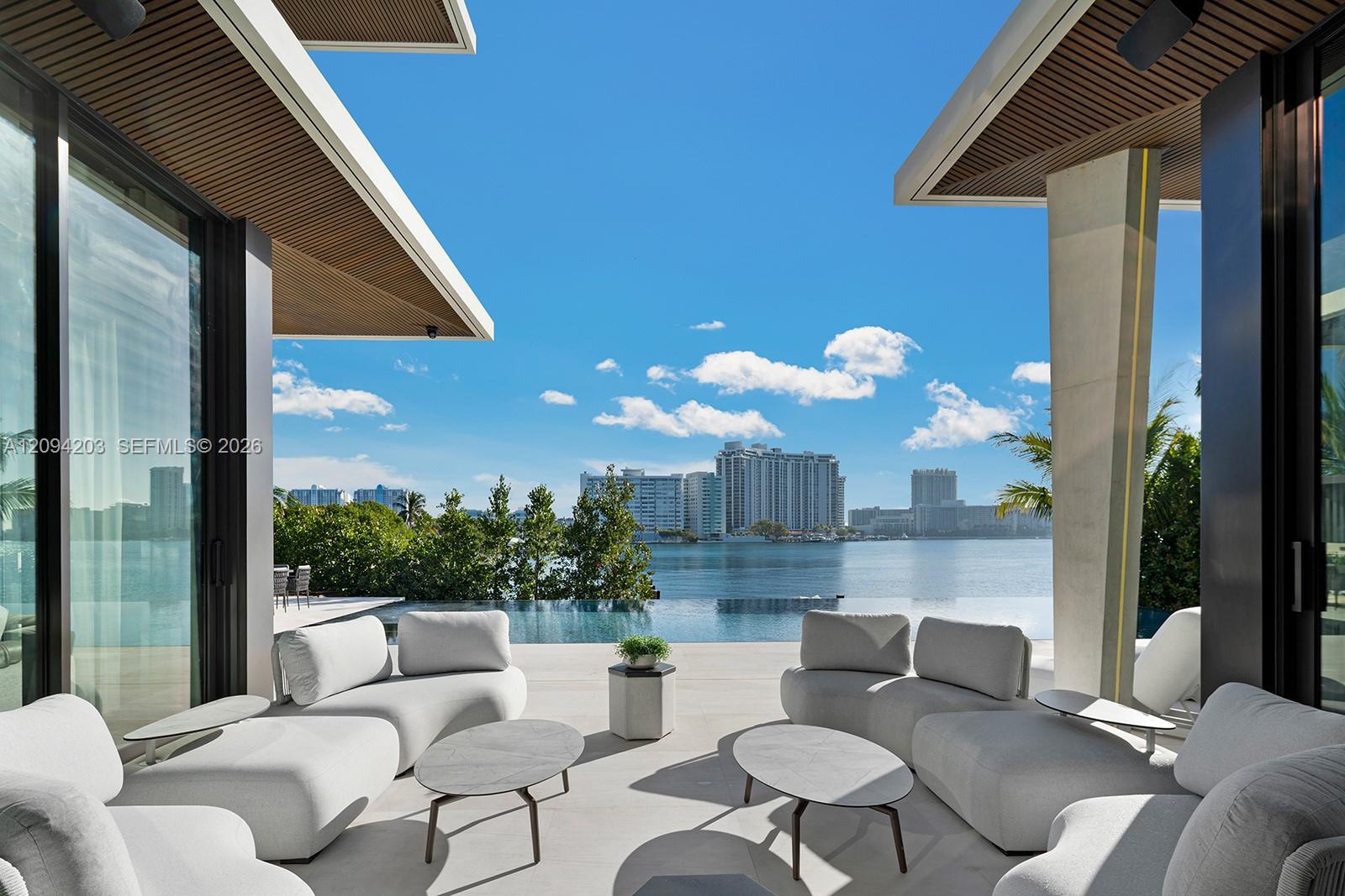 Covered terrace with white seating and an infinity pool overlooking the water and city skyline.