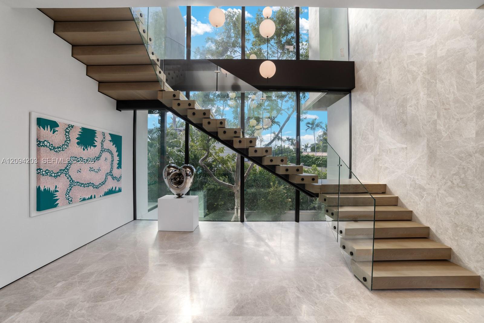 Modern foyer with a floating wood staircase, glass railings, and floor-to-ceiling windows.