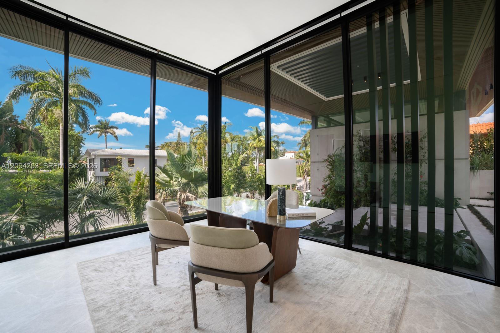 Modern dining area with floor-to-ceiling glass walls overlooking palm trees and lush landscaping.