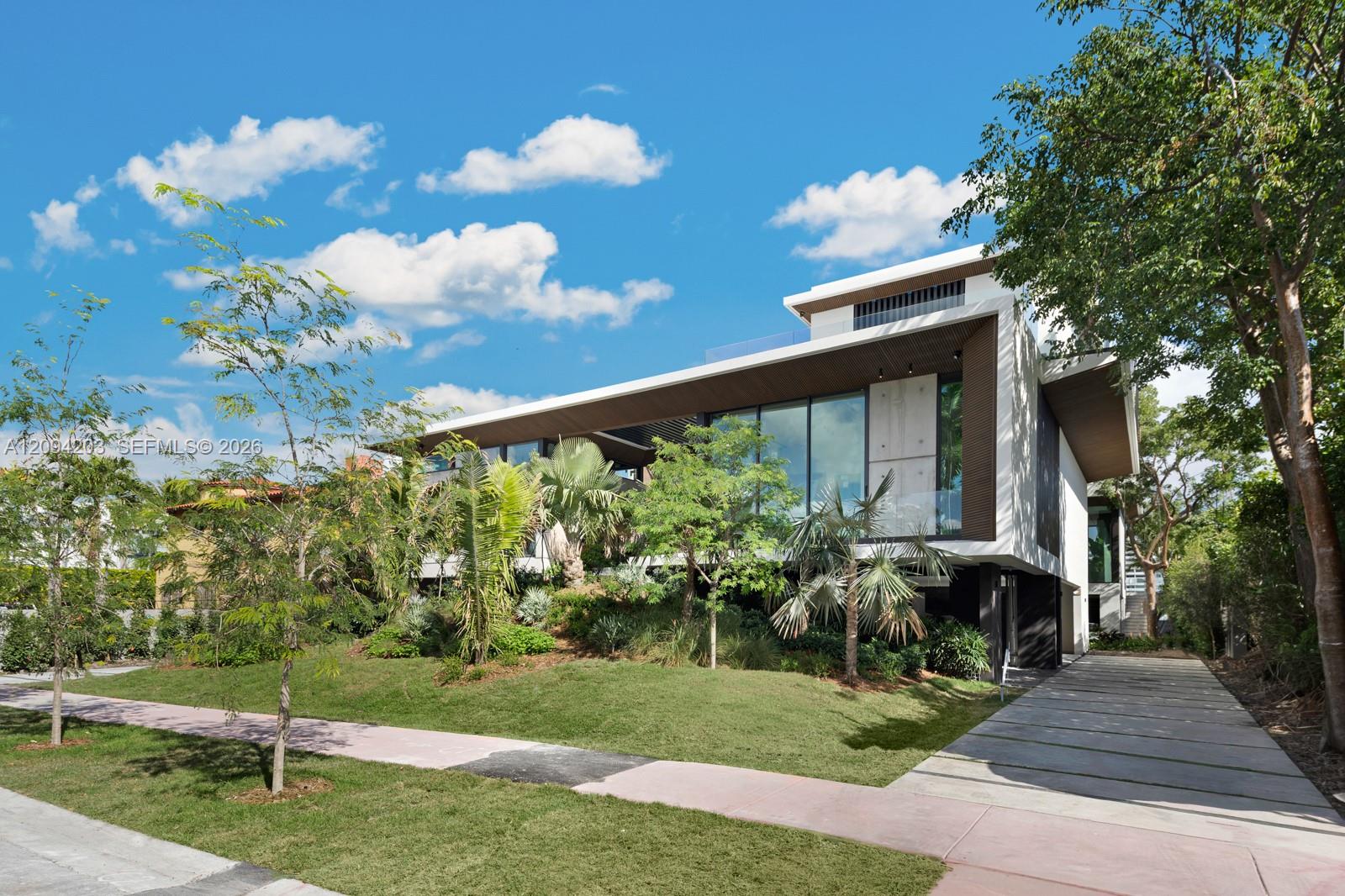 Modern two-story home with wide rooflines, expansive glass windows, and tropical landscaping along the entrance walk.