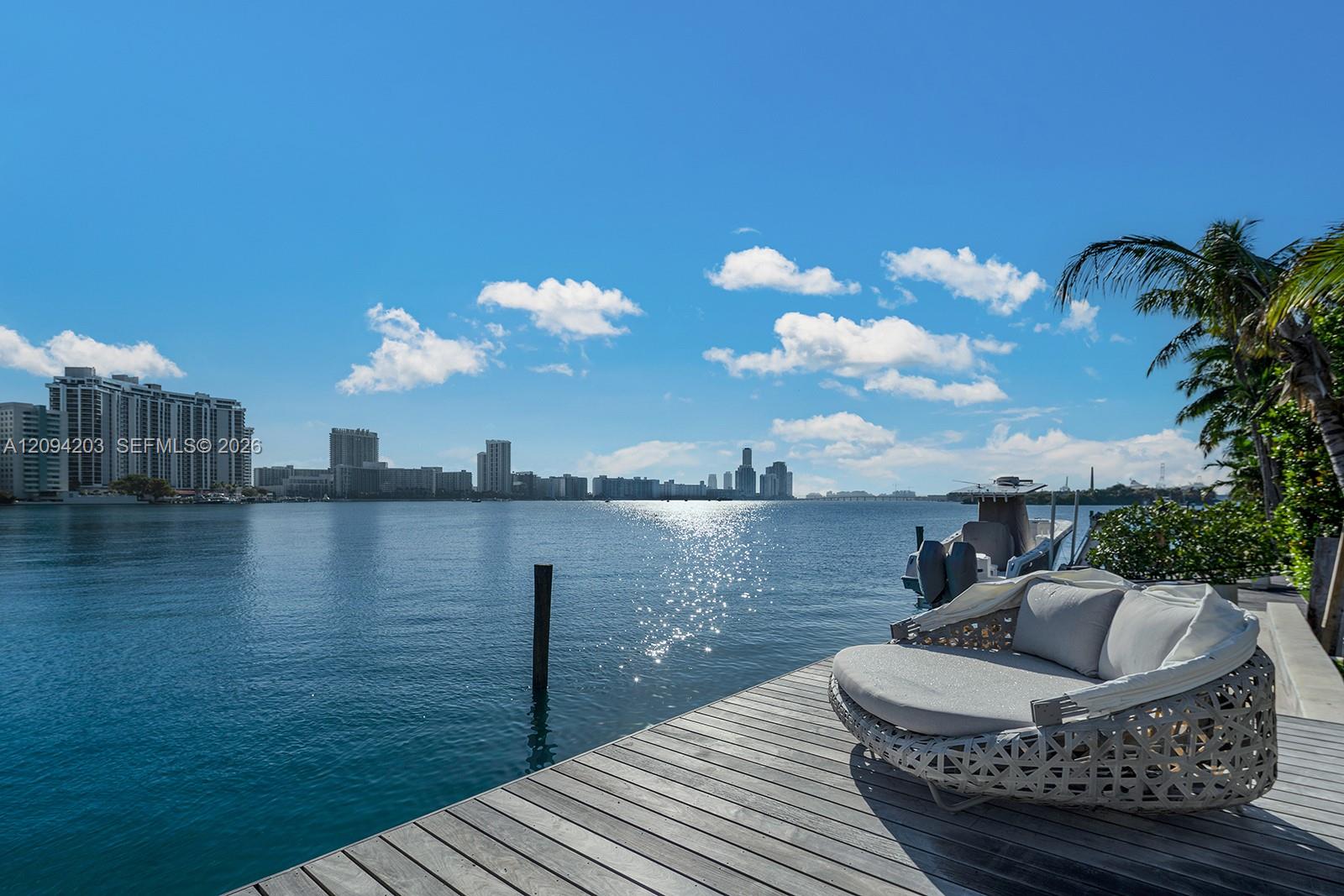 Waterfront deck with cushioned lounge seating overlooking the bay and distant Miami skyline.