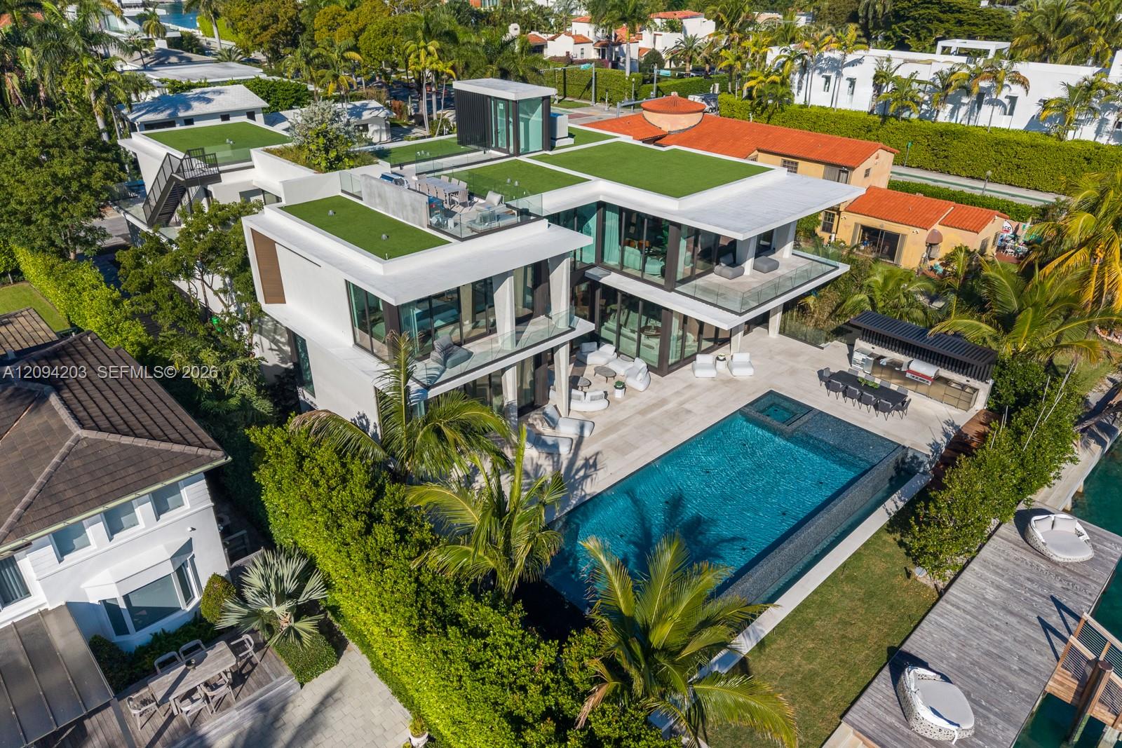 Modern white home with green rooftop terraces, glass balconies, and a long backyard pool.