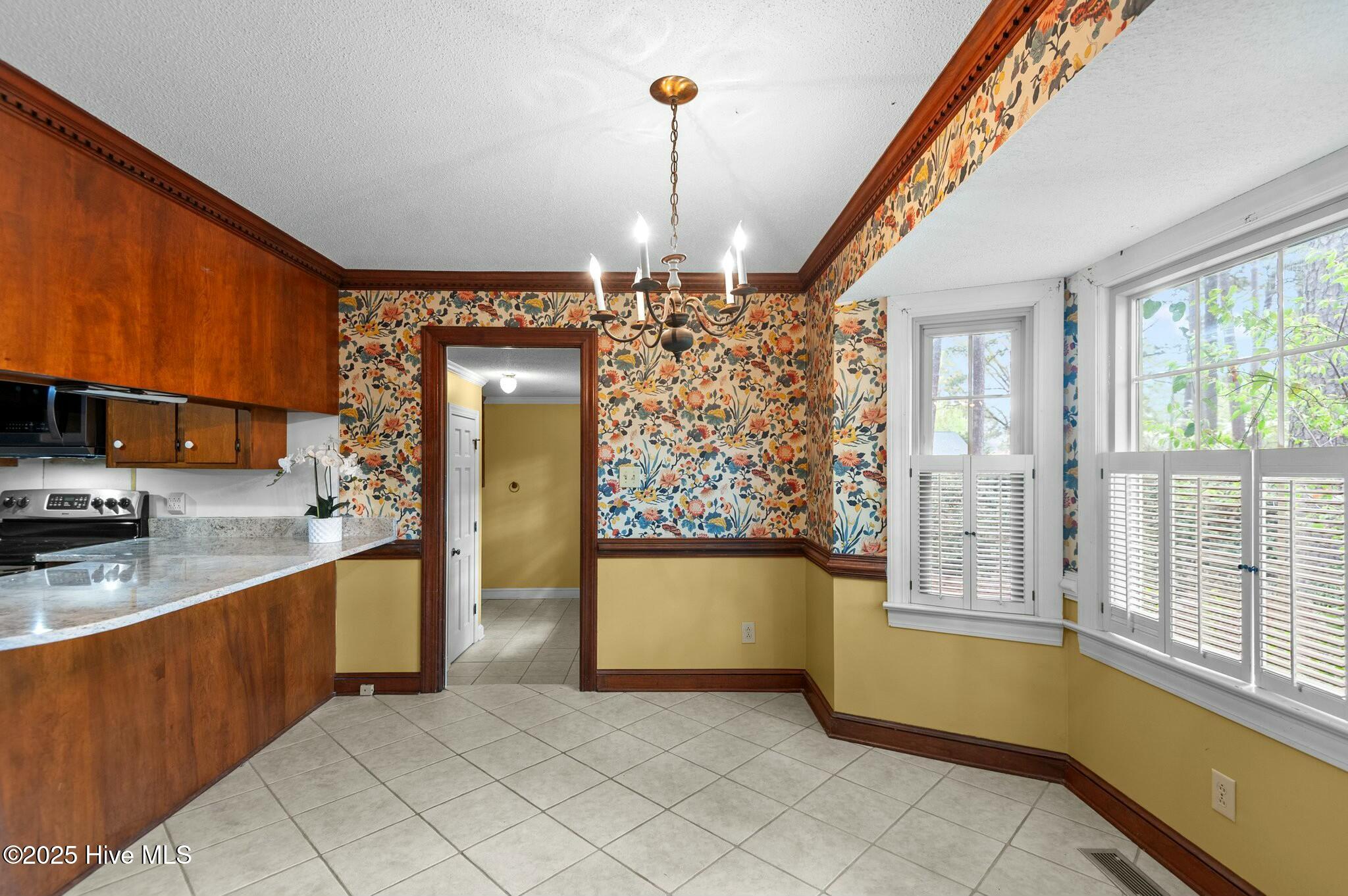 Kitchen and dining area with floral wallpaper, wood cabinets, tile floors, and shuttered windows.
