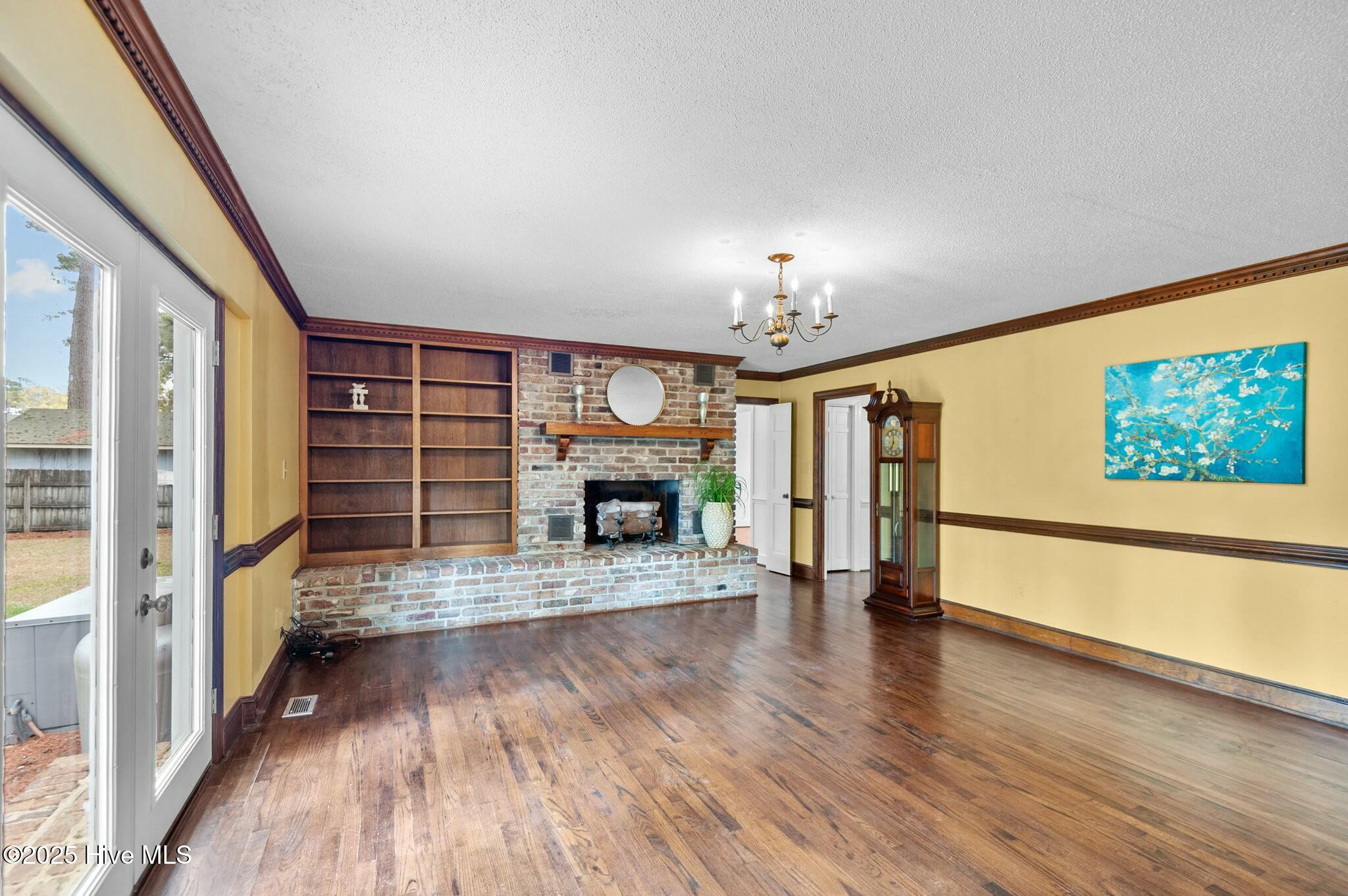 Living room with a brick fireplace, built-in bookcase, hardwood floors, and French doors.