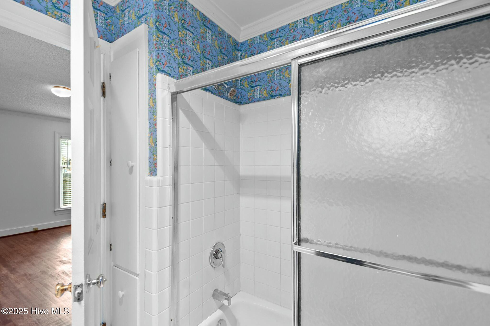 Bathroom with white tiled tub and shower, frosted-glass door, and blue floral wallpaper.