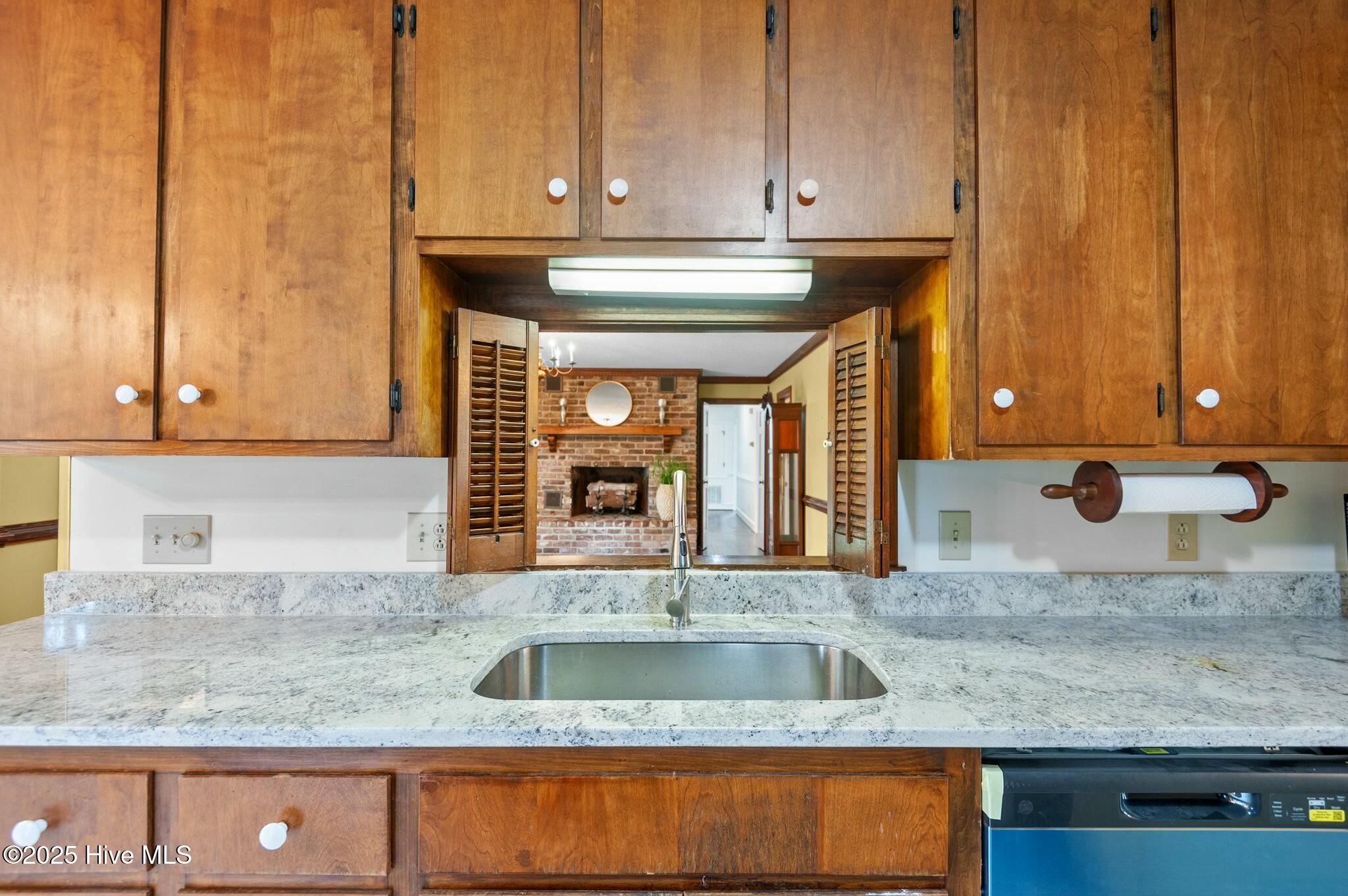 Kitchen with wood cabinets and granite counters, looking through a pass-through toward a brick fireplace.