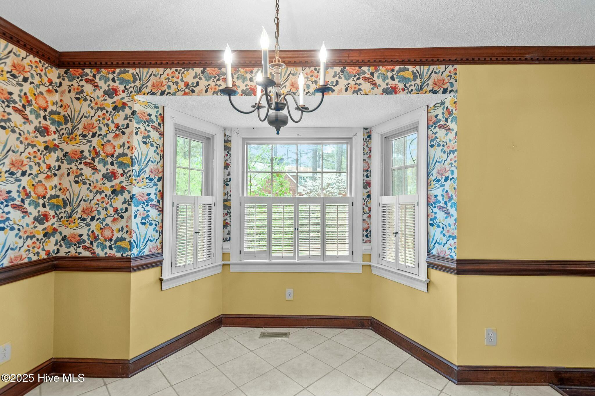Dining nook with a shuttered bay window, bold floral wallpaper, yellow walls, and a chandelier.