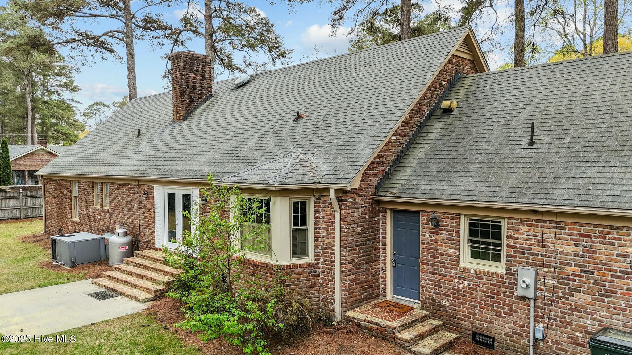 Red brick house with a gray shingle roof, blue side door, and brick steps.