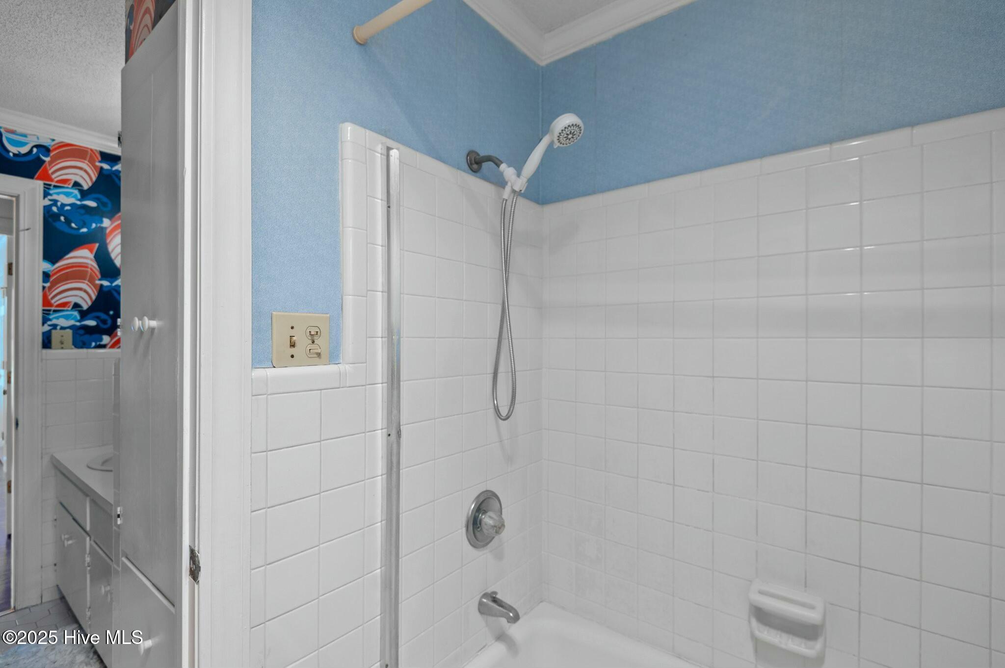 White tiled bathtub and shower with a handheld showerhead and blue walls.