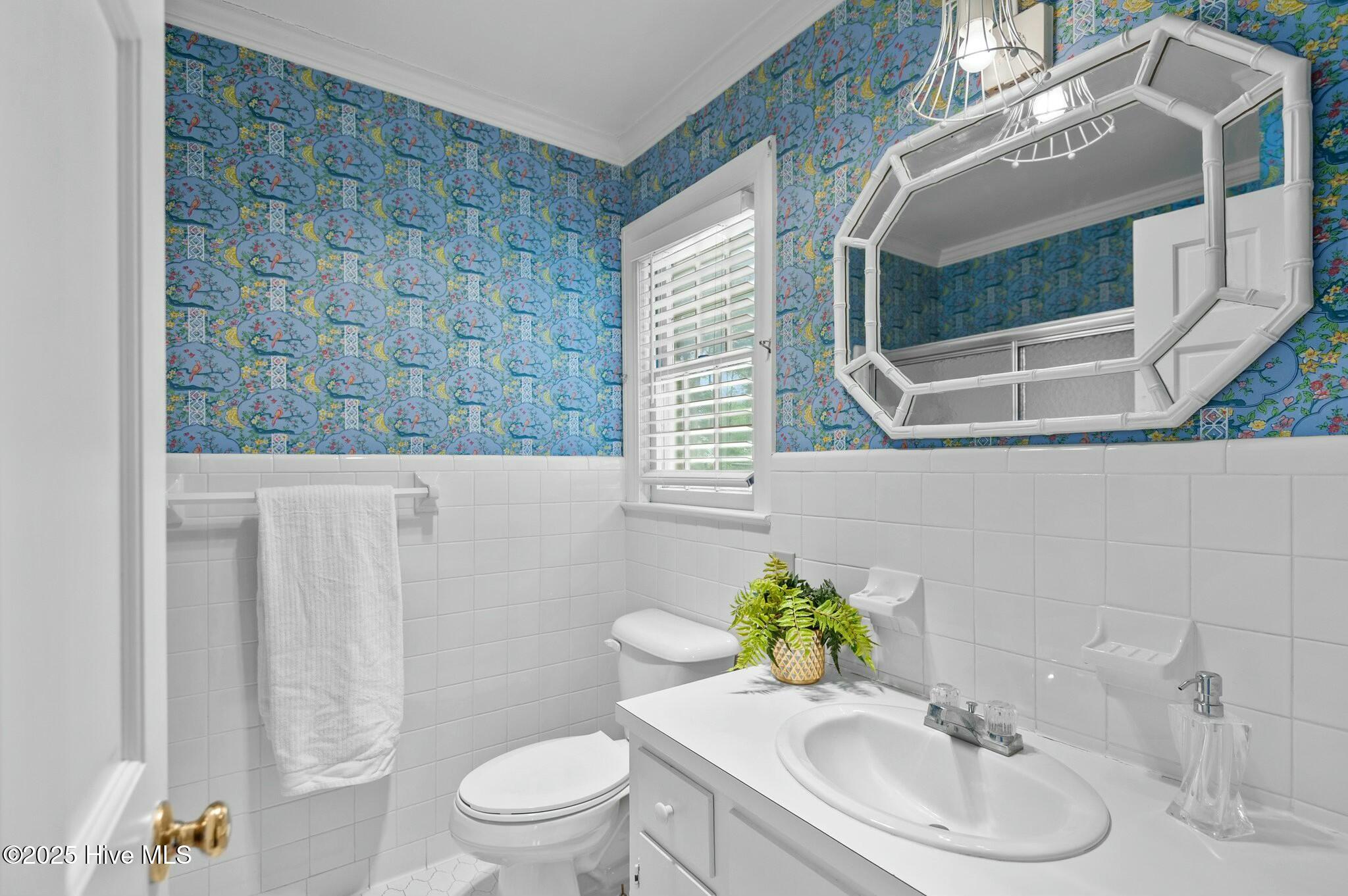 Bathroom with blue patterned wallpaper, white tile, and a large geometric mirror.