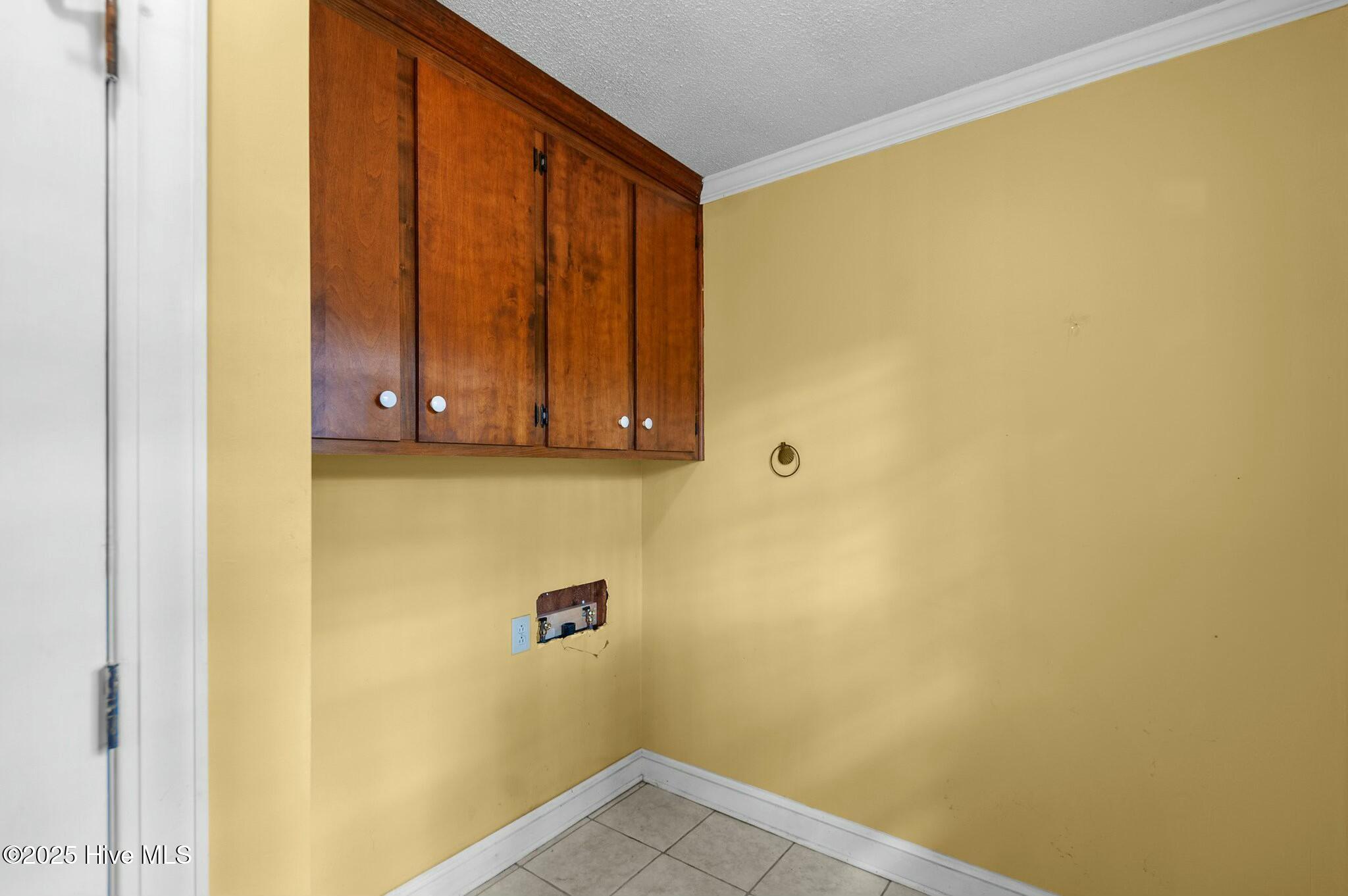 Empty laundry area with upper wood cabinets, exposed washer hookups, and beige tile flooring.