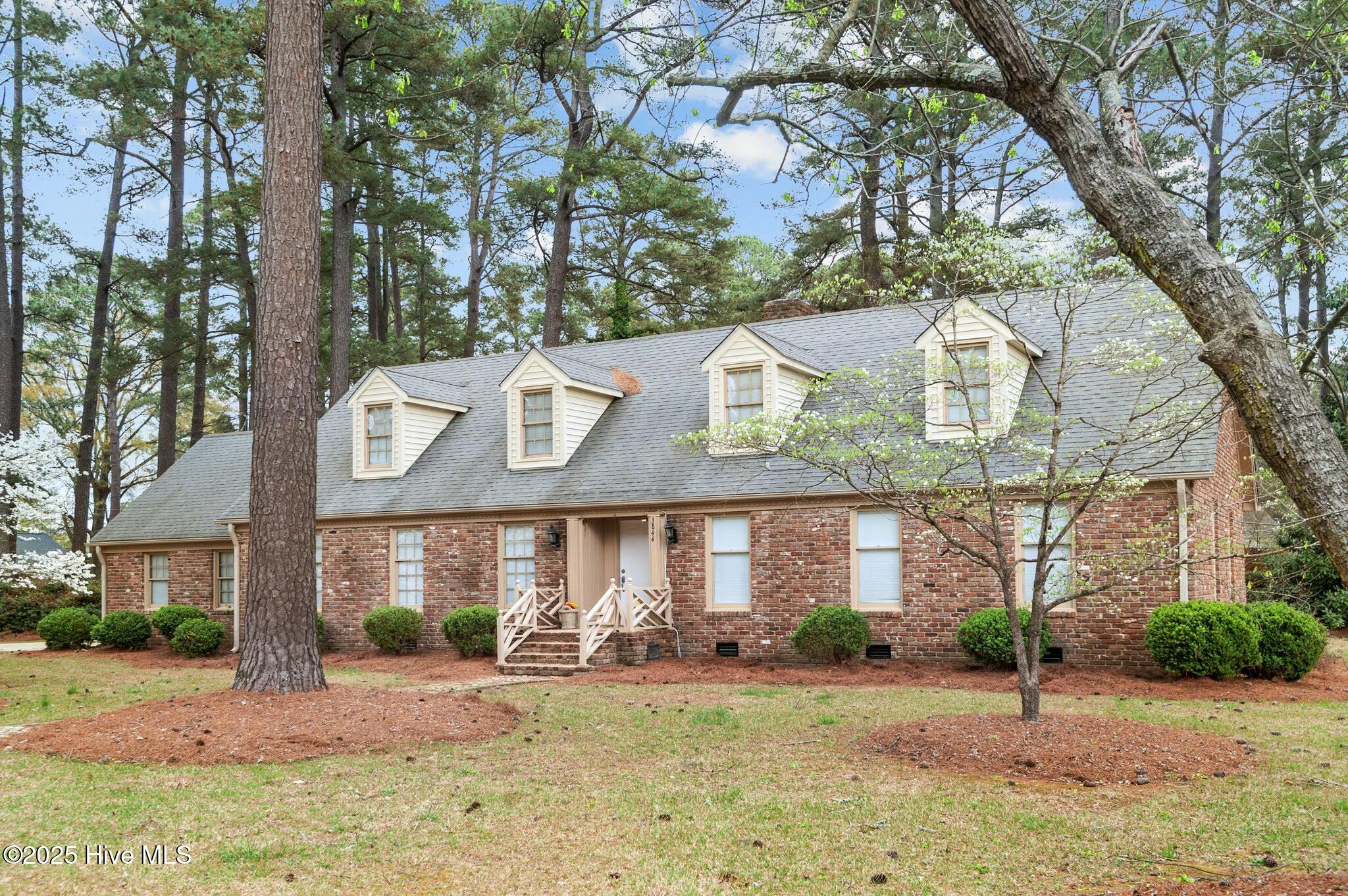 Red-brick house with three roof dormers and a small wooden entry porch, framed by mature trees.