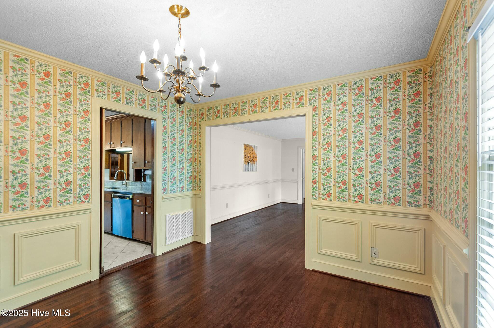 Dining room with floral wallpaper, pale green paneling, brass chandelier, and dark hardwood floors.