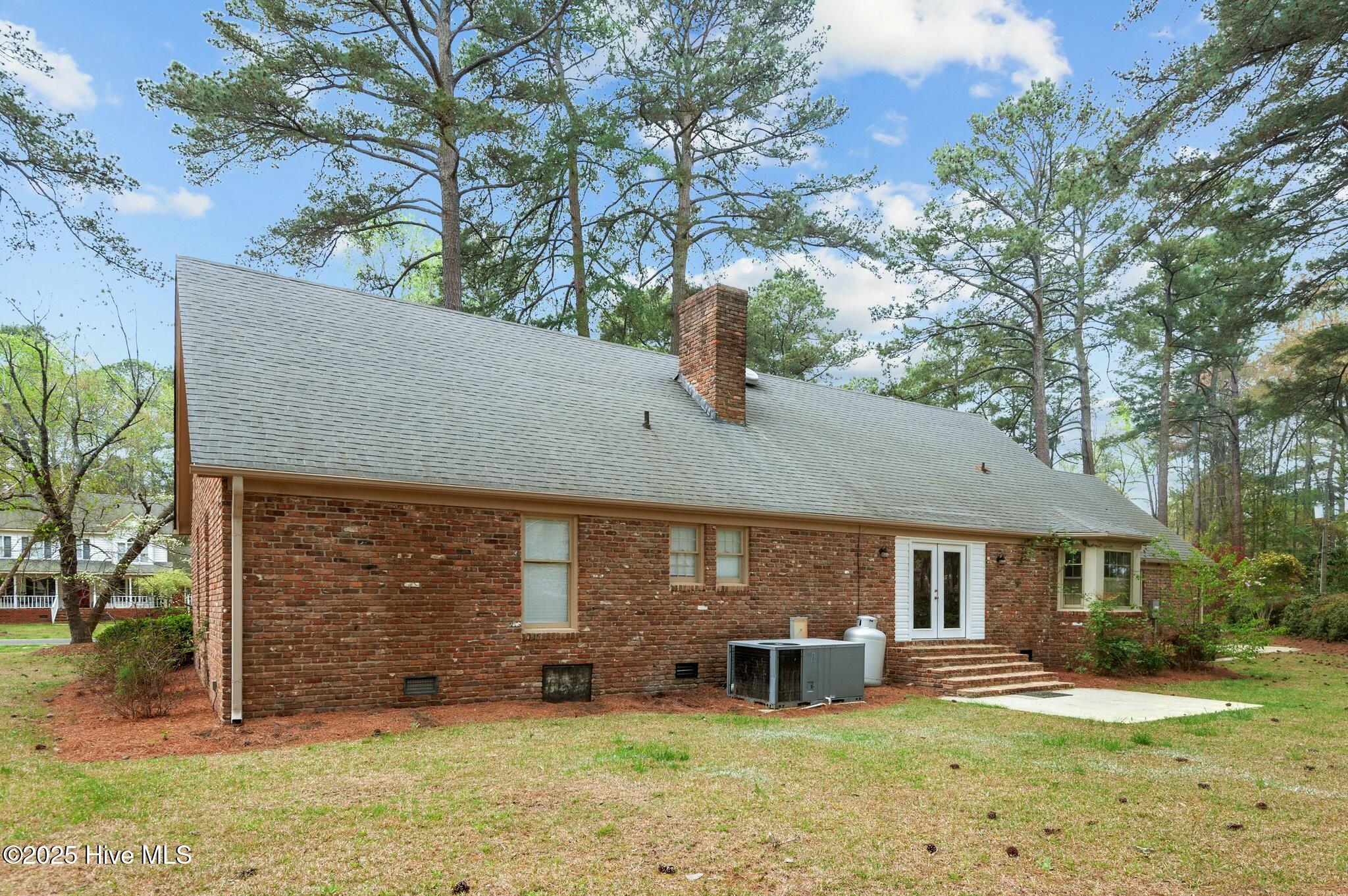 Rear of a red brick house with a long gray roof, chimney, and white French doors.