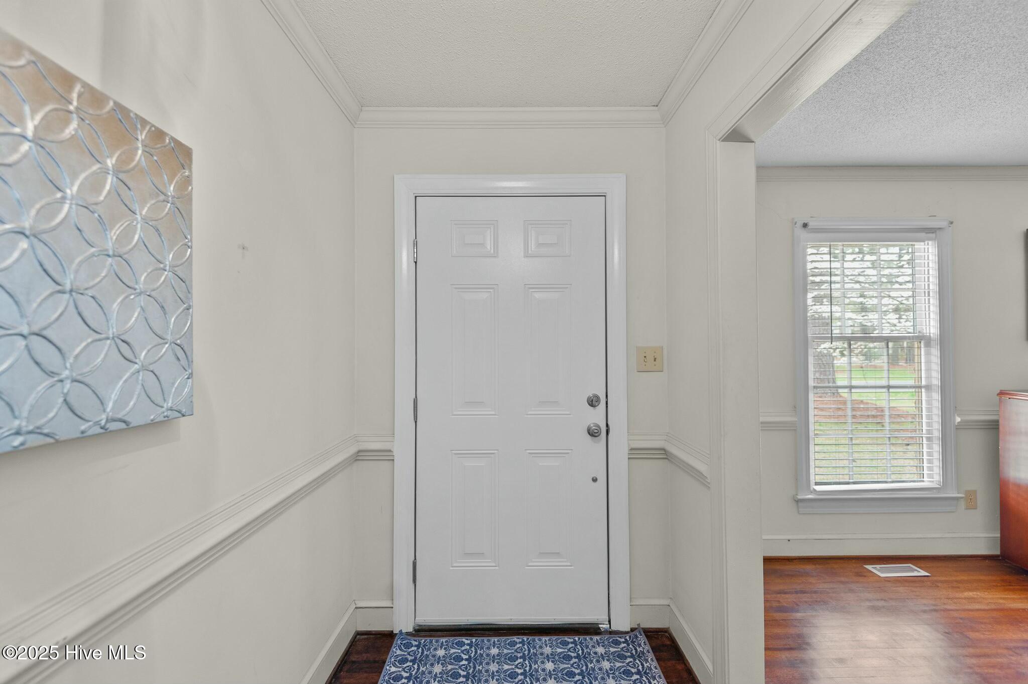 Entry foyer with a white paneled front door, blue wall art, and patterned doormat.