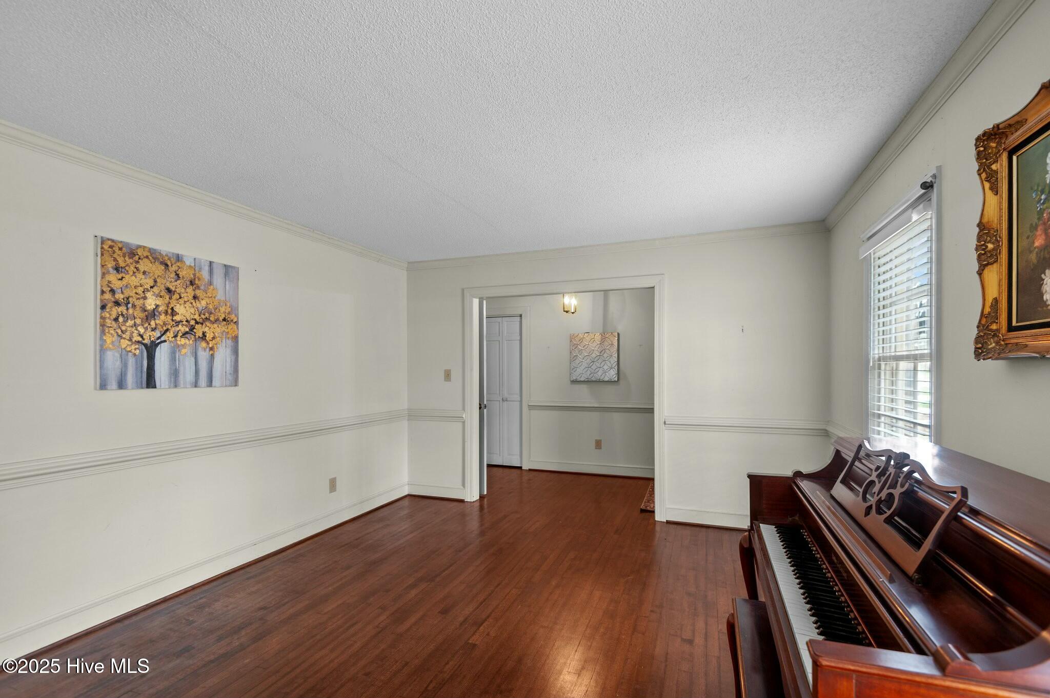 Room with hardwood floors and a dark wood piano beside a window.