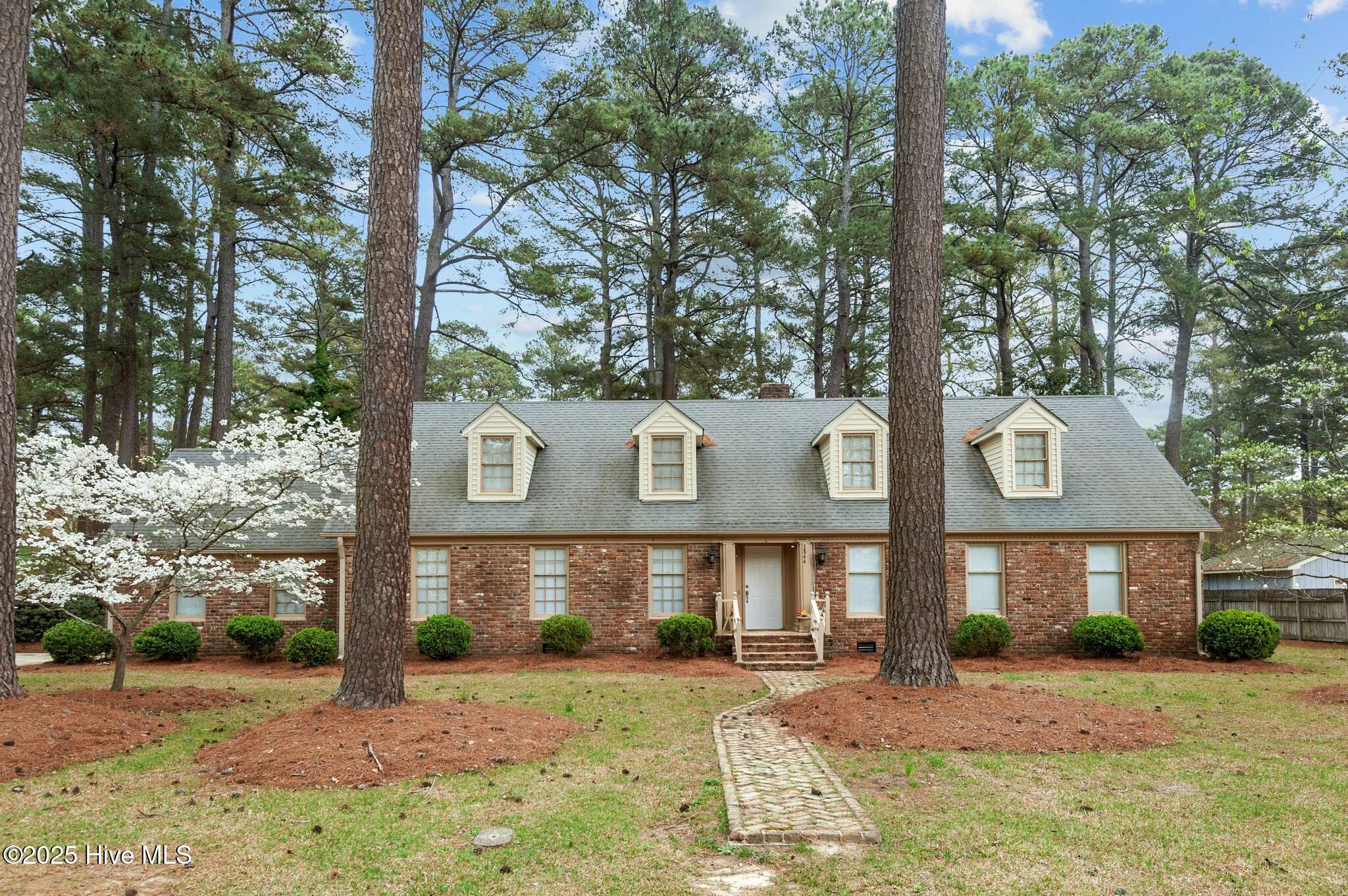 Red-brick house with four dormers, tall pines, and a stone walkway to the front entrance.