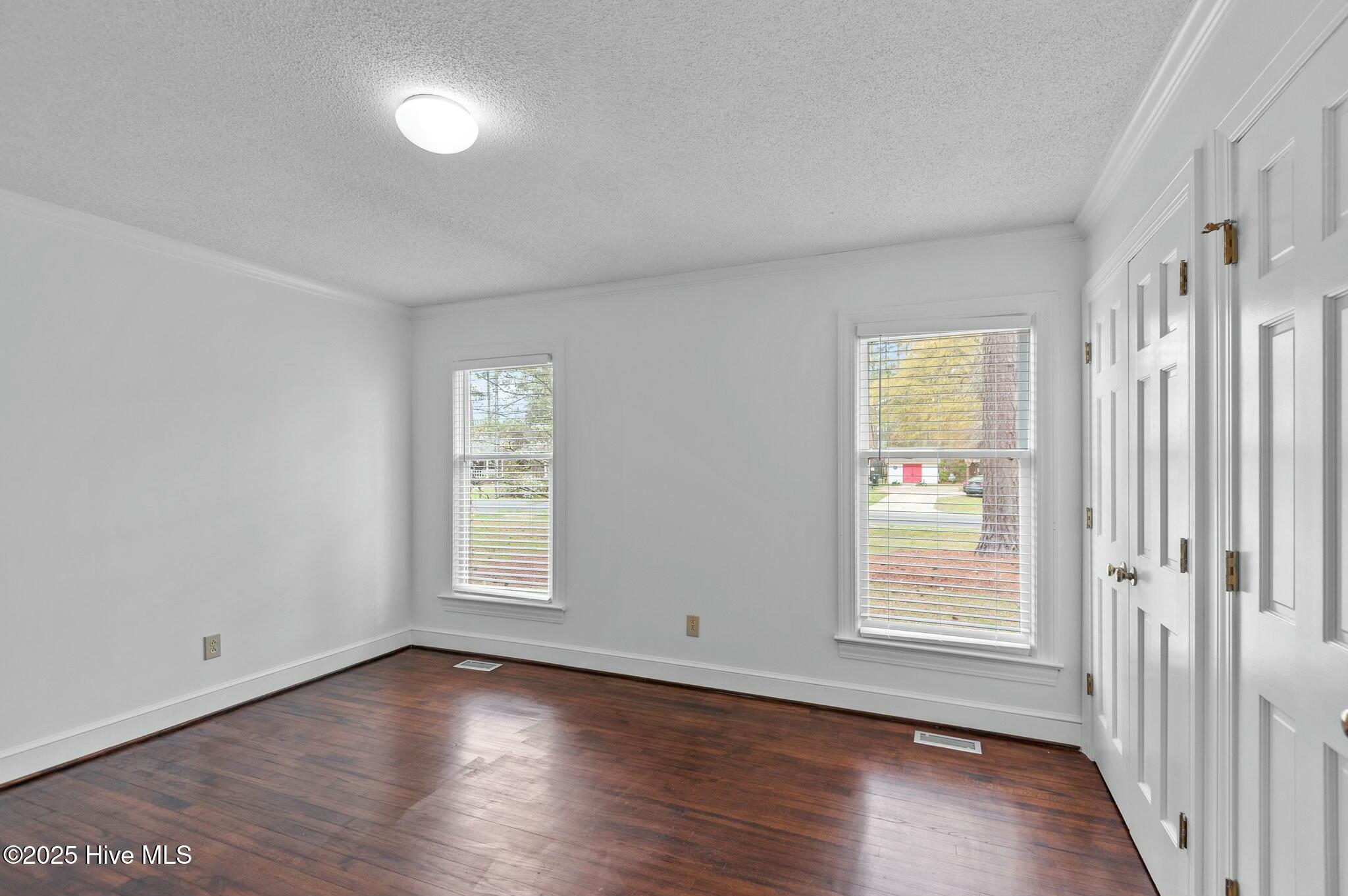 Vacant bedroom with dark hardwood floors, two windows, and white closet doors.