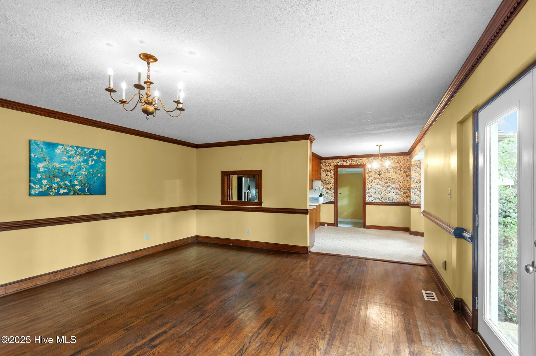 Unfurnished room with polished hardwood floors, yellow walls, dark wood trim, and a brass chandelier.