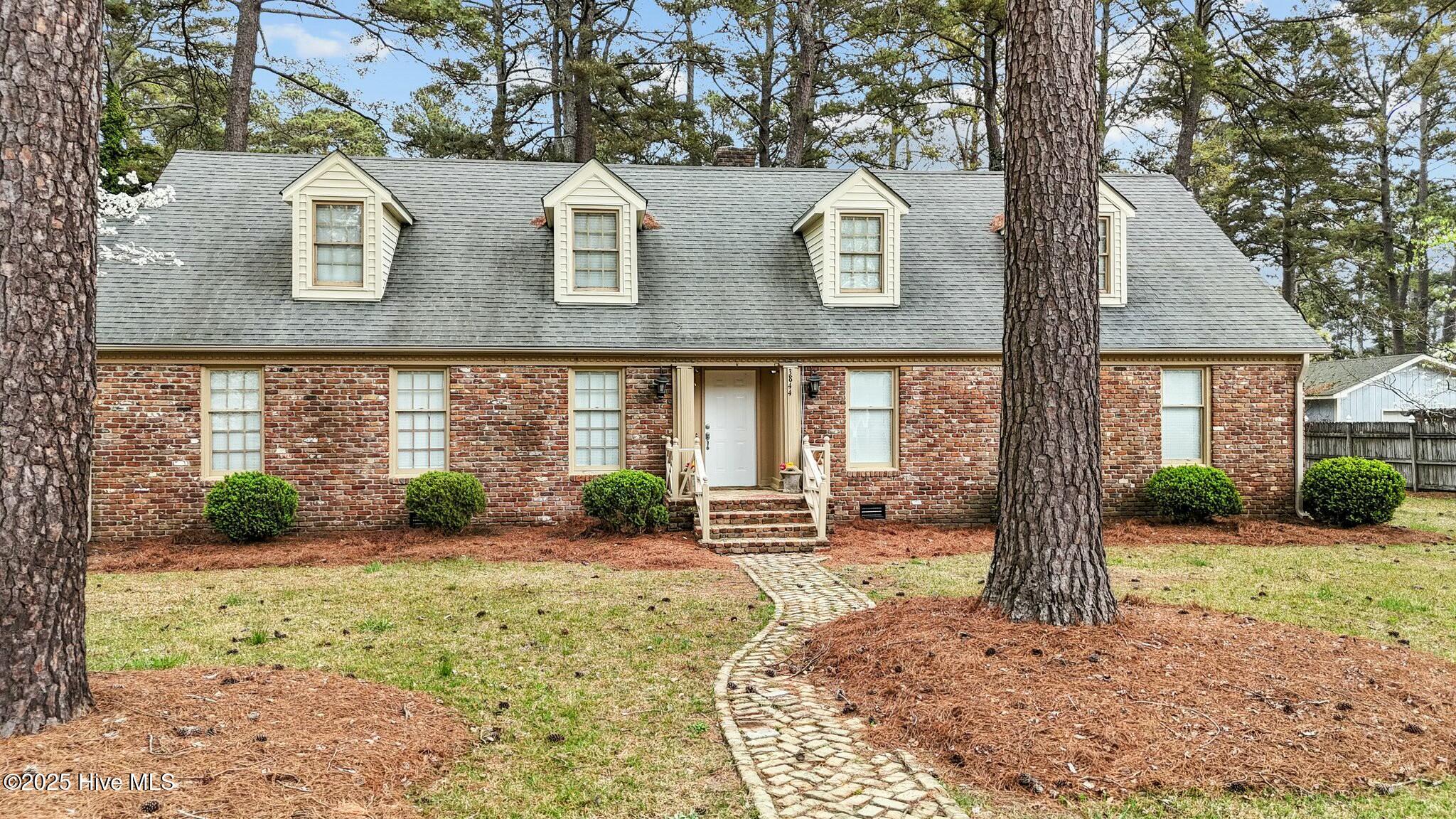 Brick house with four dormers, framed by pine trees and approached by a curved stone walkway.
