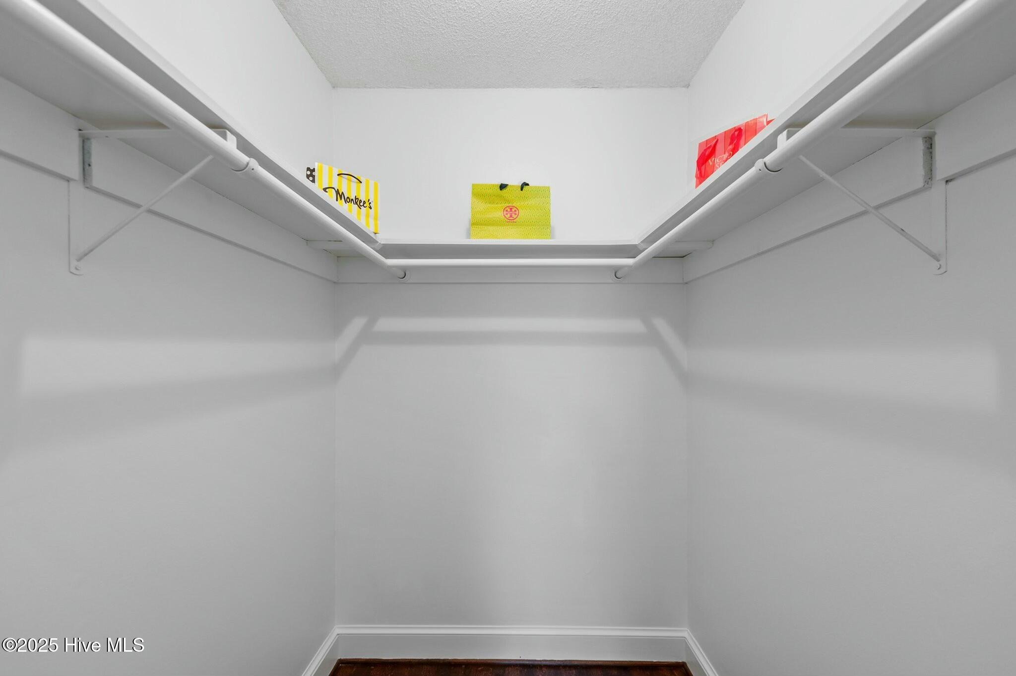 Walk-in closet with wraparound hanging rods, upper shelves, and shopping bags on the back shelf.