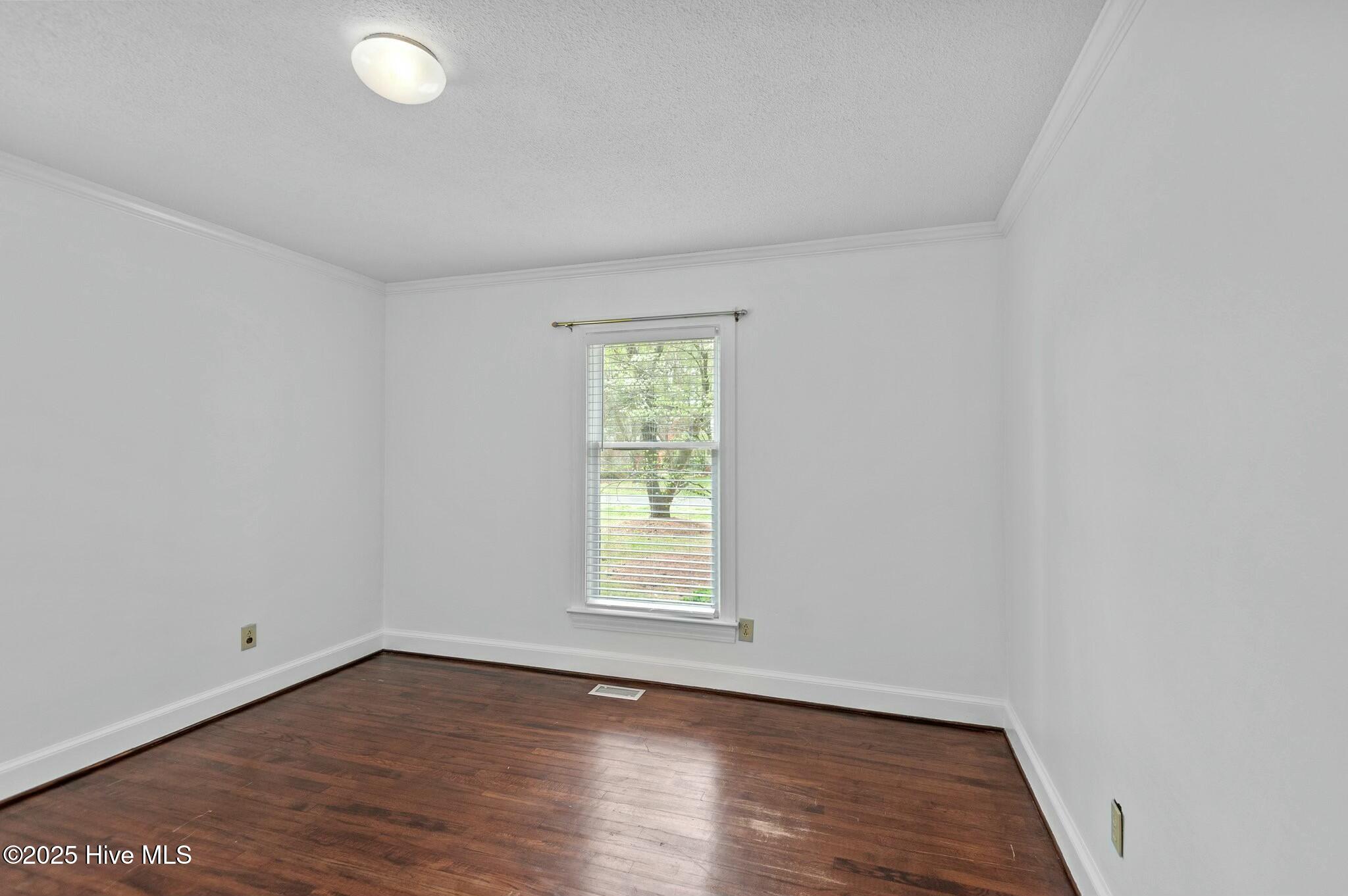 Empty room with dark hardwood floors, white walls, and a window with blinds.