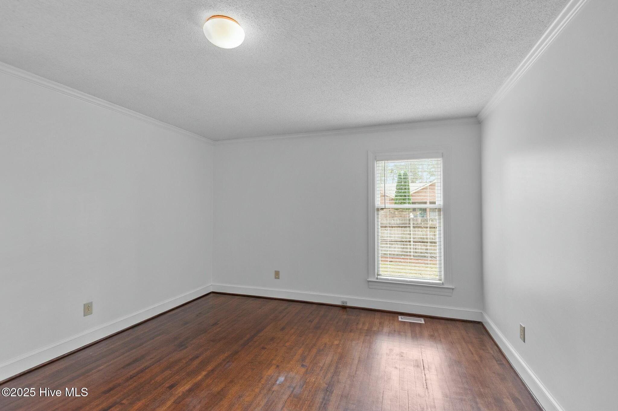 Empty room with dark hardwood floors, white walls, and a single window with blinds.