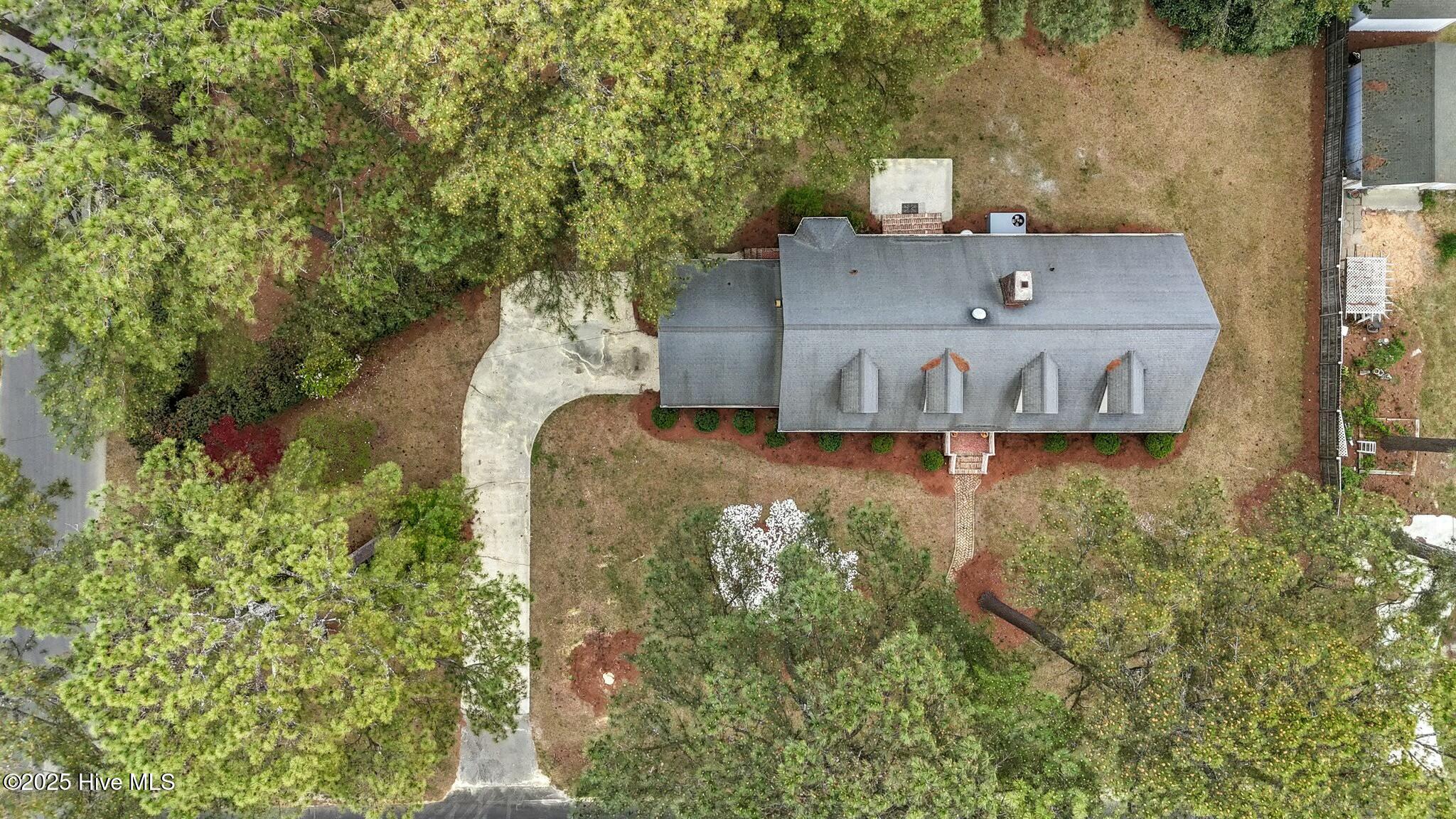 Aerial view of a home with a long gray roof, curved driveway, and mature trees.