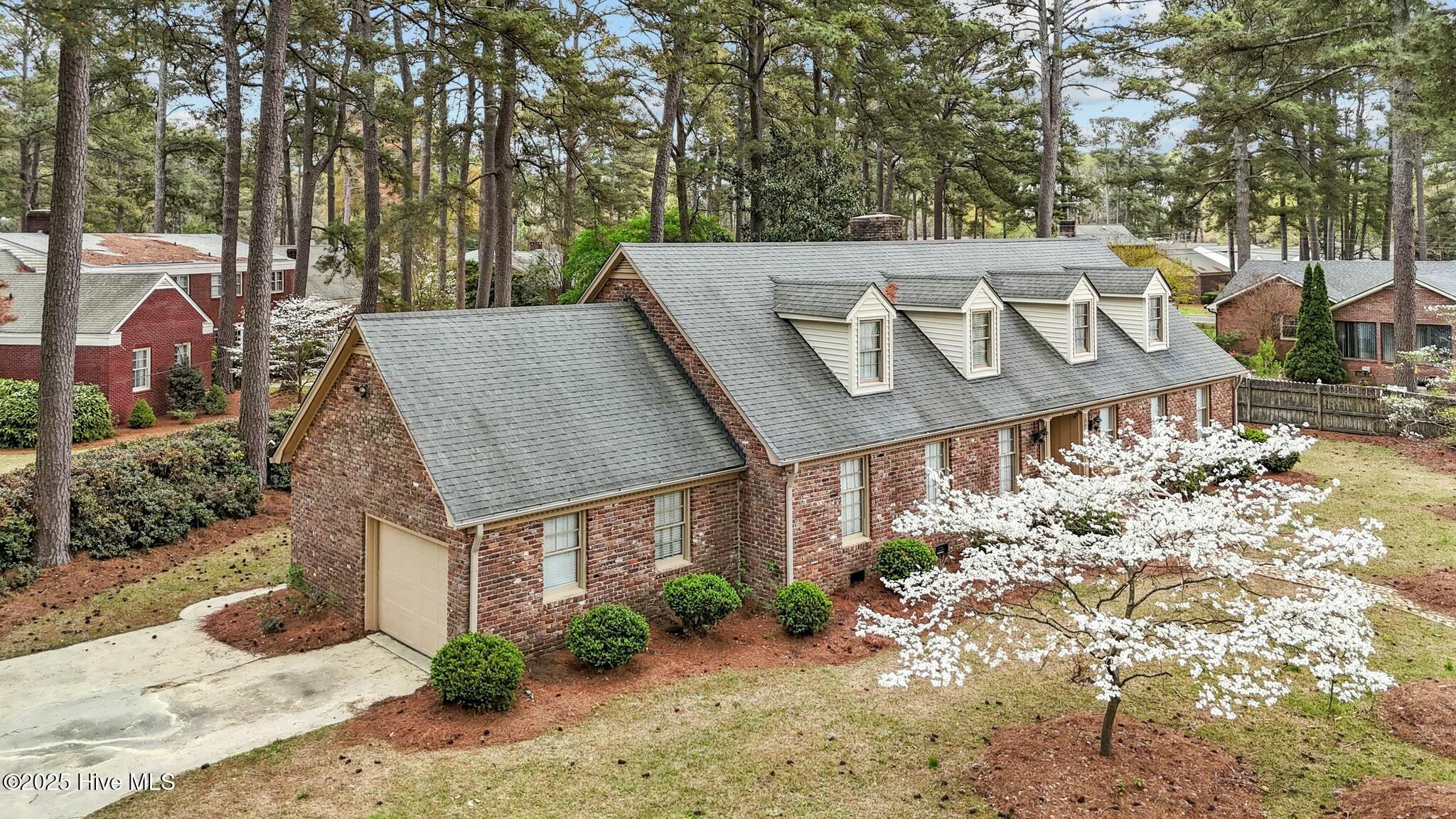 Brick house with four roof dormers, surrounded by tall pines and flowering dogwood.
