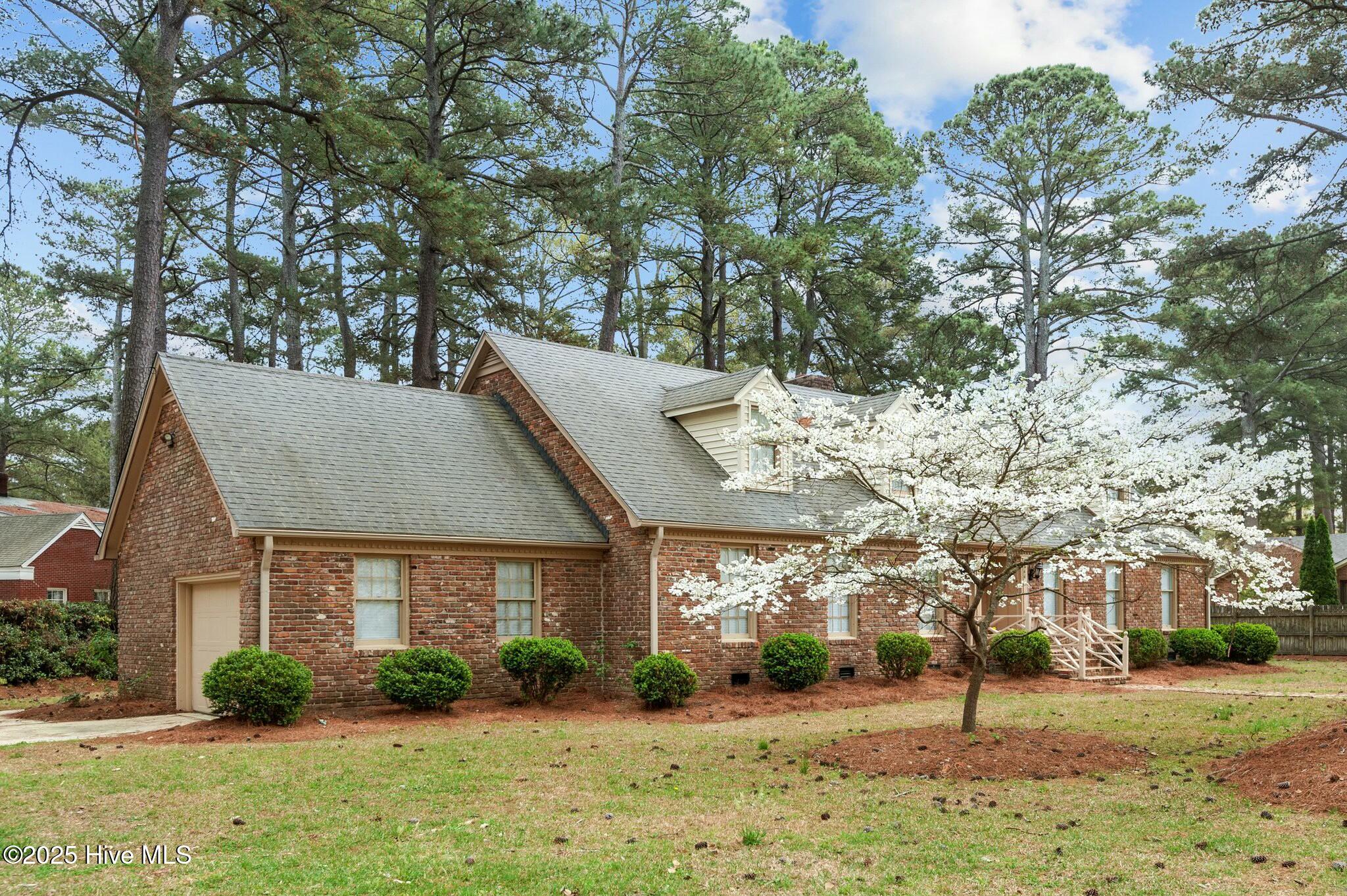Red brick house with a gray gabled roof and a white-flowering tree in the yard.