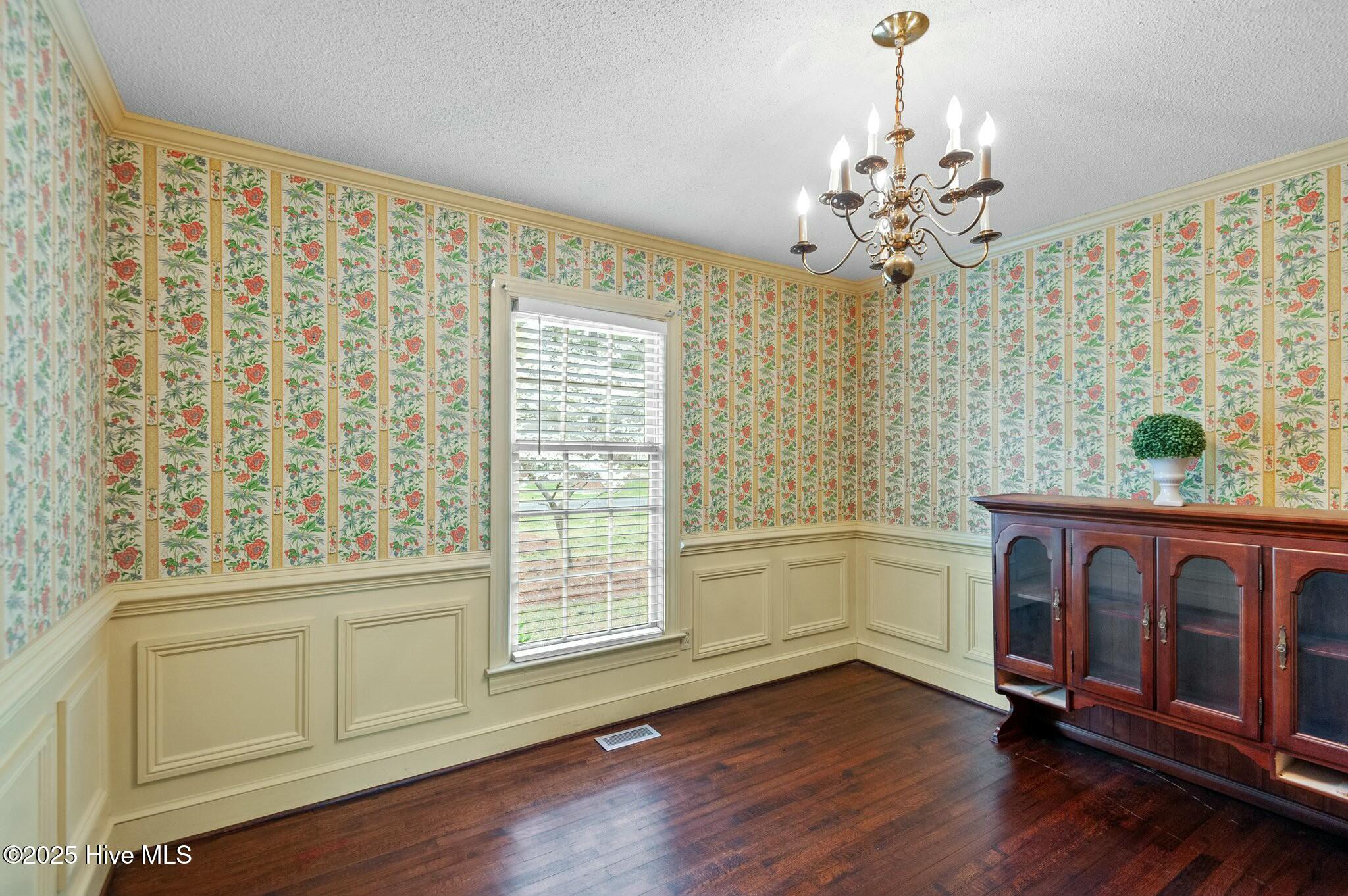 Dining room with floral wallpaper, cream wainscoting, a brass chandelier, and a dark wood cabinet.