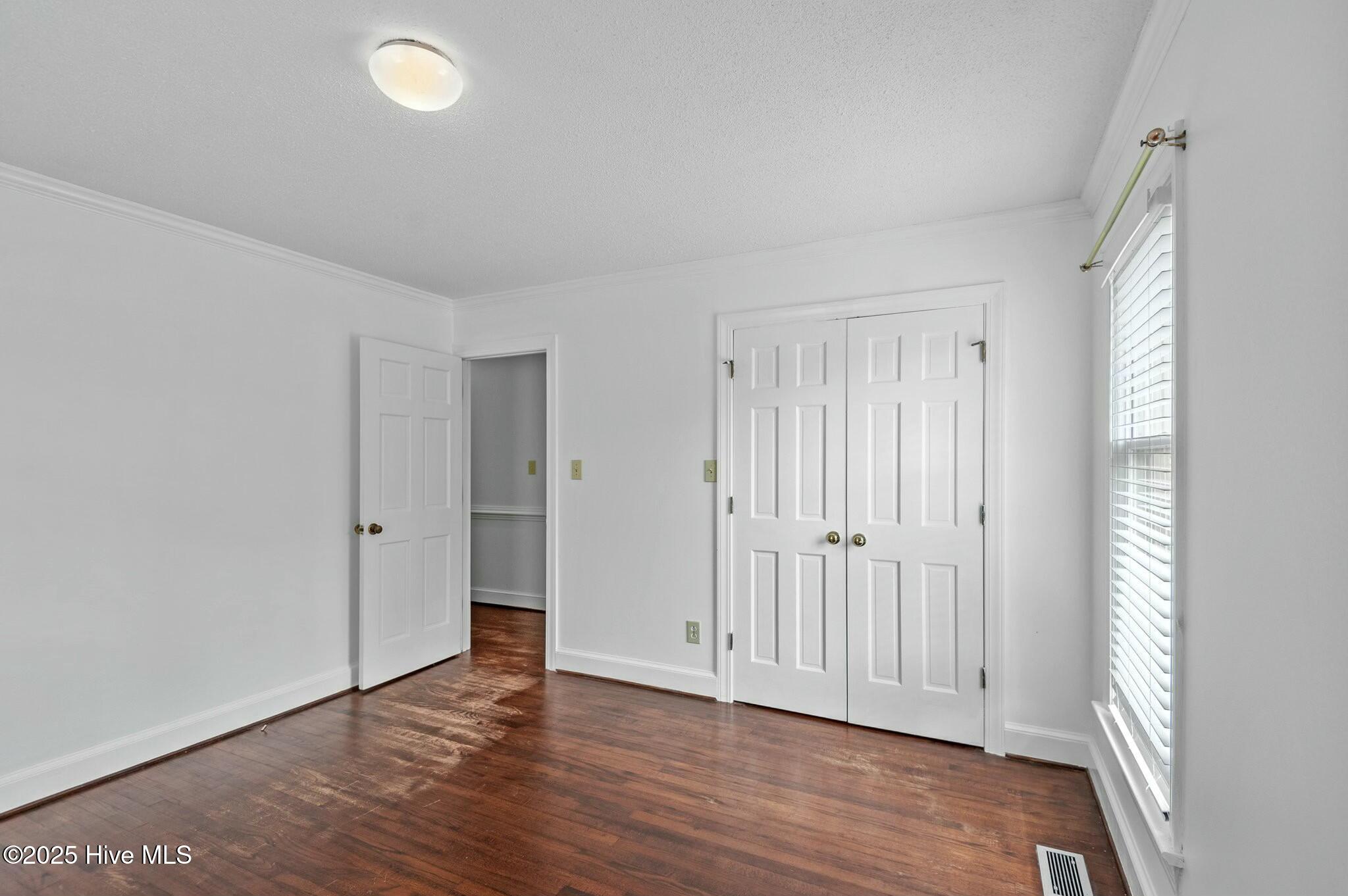 Empty room with hardwood floors, double closet doors, and a window with blinds.