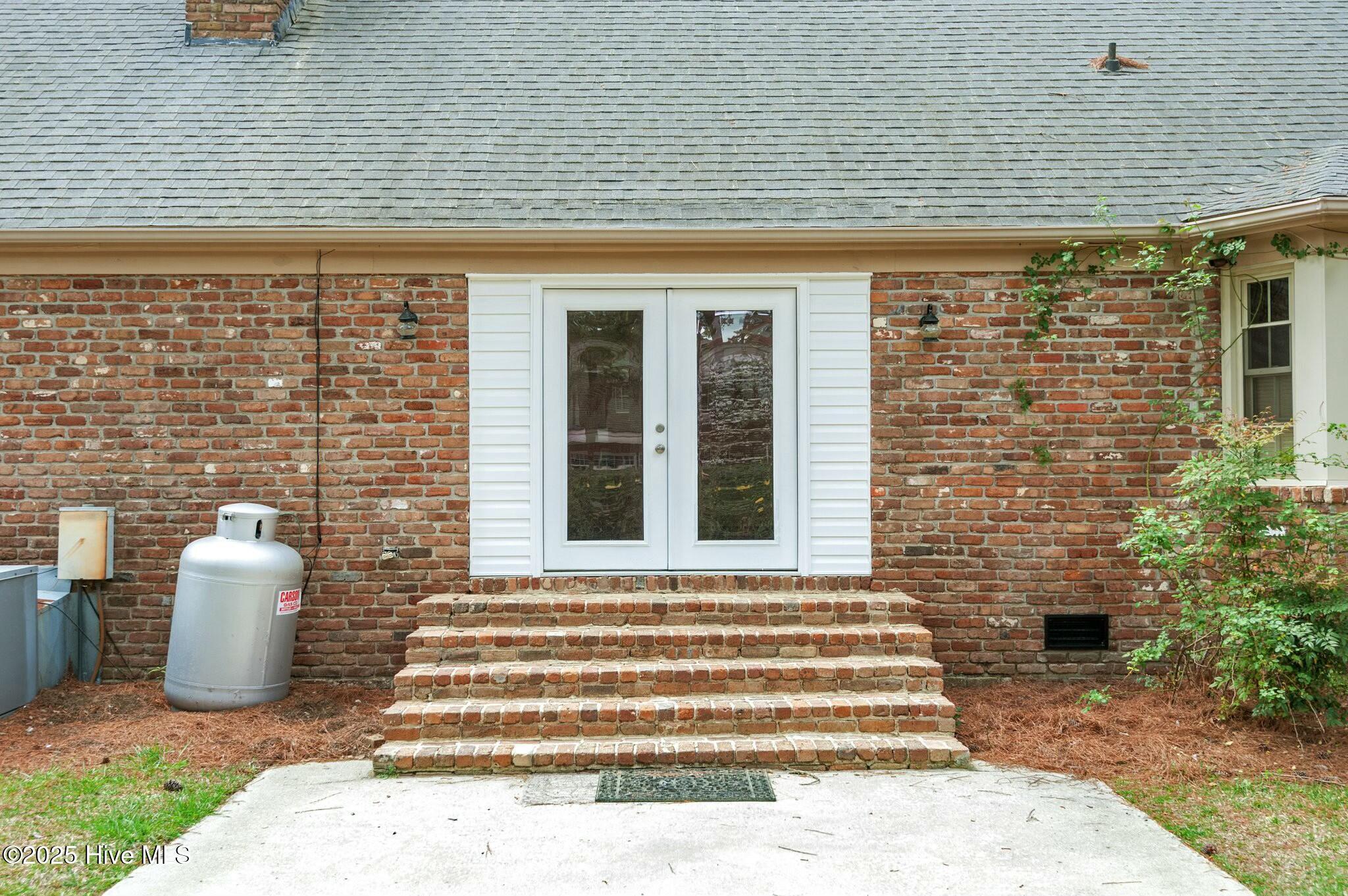 Brick house exterior with white double doors, brick steps, and a propane tank beside the patio.