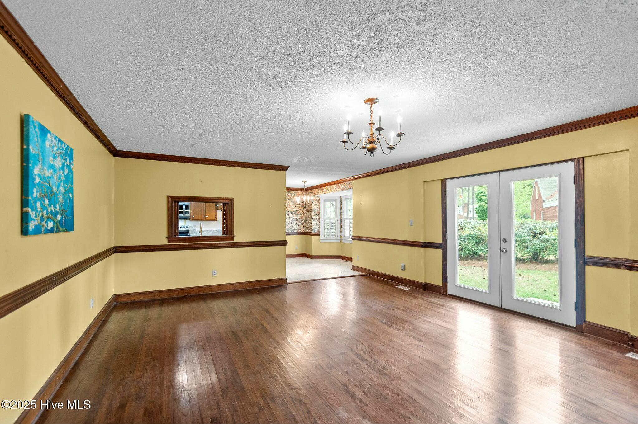 Empty room with hardwood floors, yellow walls, a kitchen pass-through, and glass double doors to the yard.