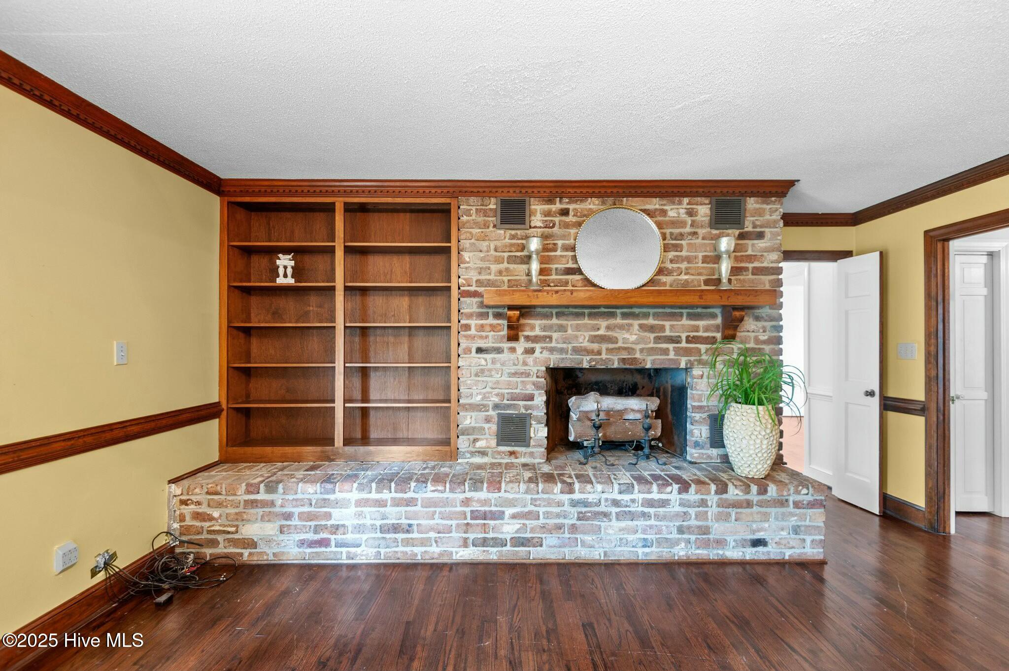 Living room with a brick fireplace, raised hearth, built-in bookshelves, and hardwood floors.