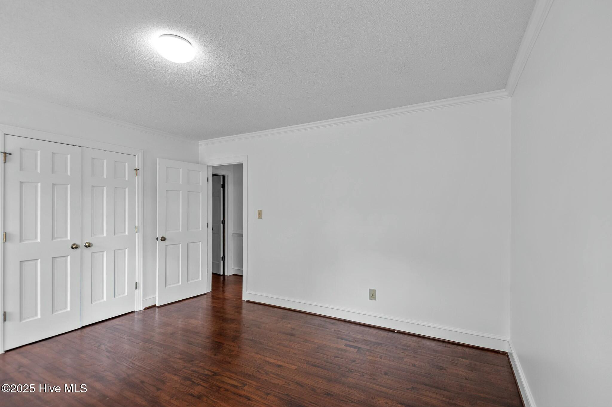 Vacant bedroom with dark hardwood floors, double closet doors, and white crown molding.