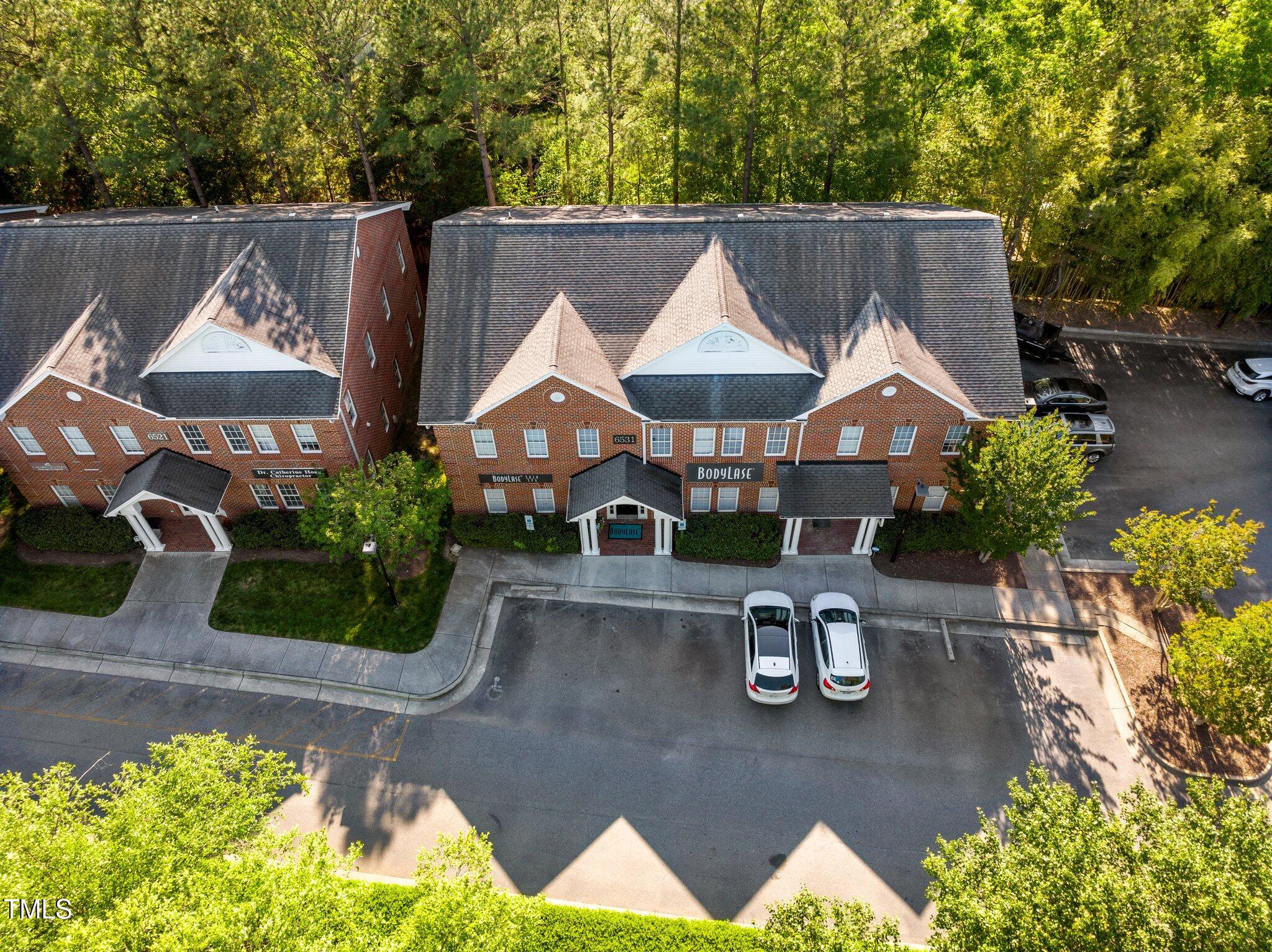 Aerial view of a red-brick building with gabled roofs, front parking, and mature trees behind it.