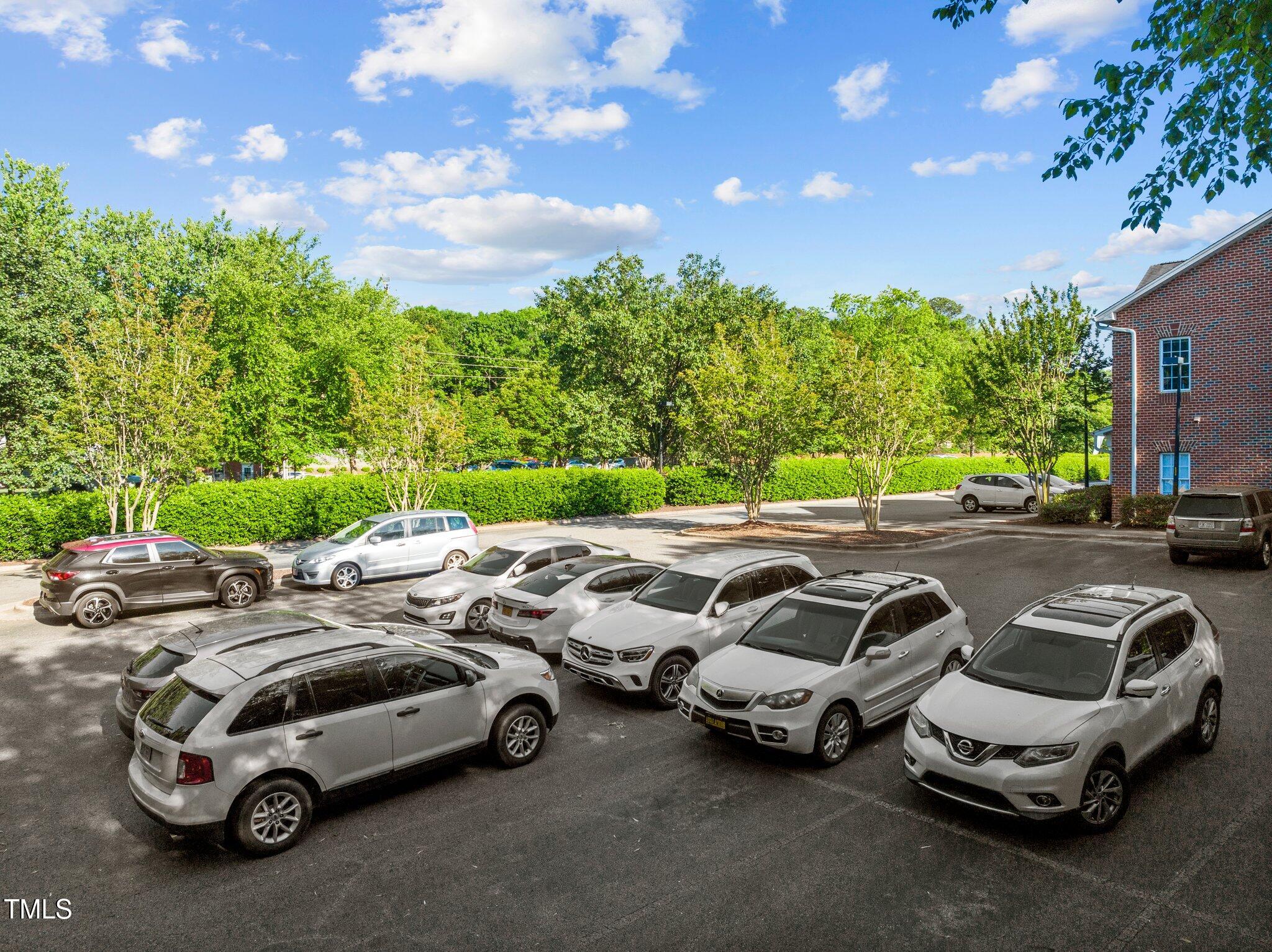 Residential parking lot with parked cars, leafy trees, and a brick building.