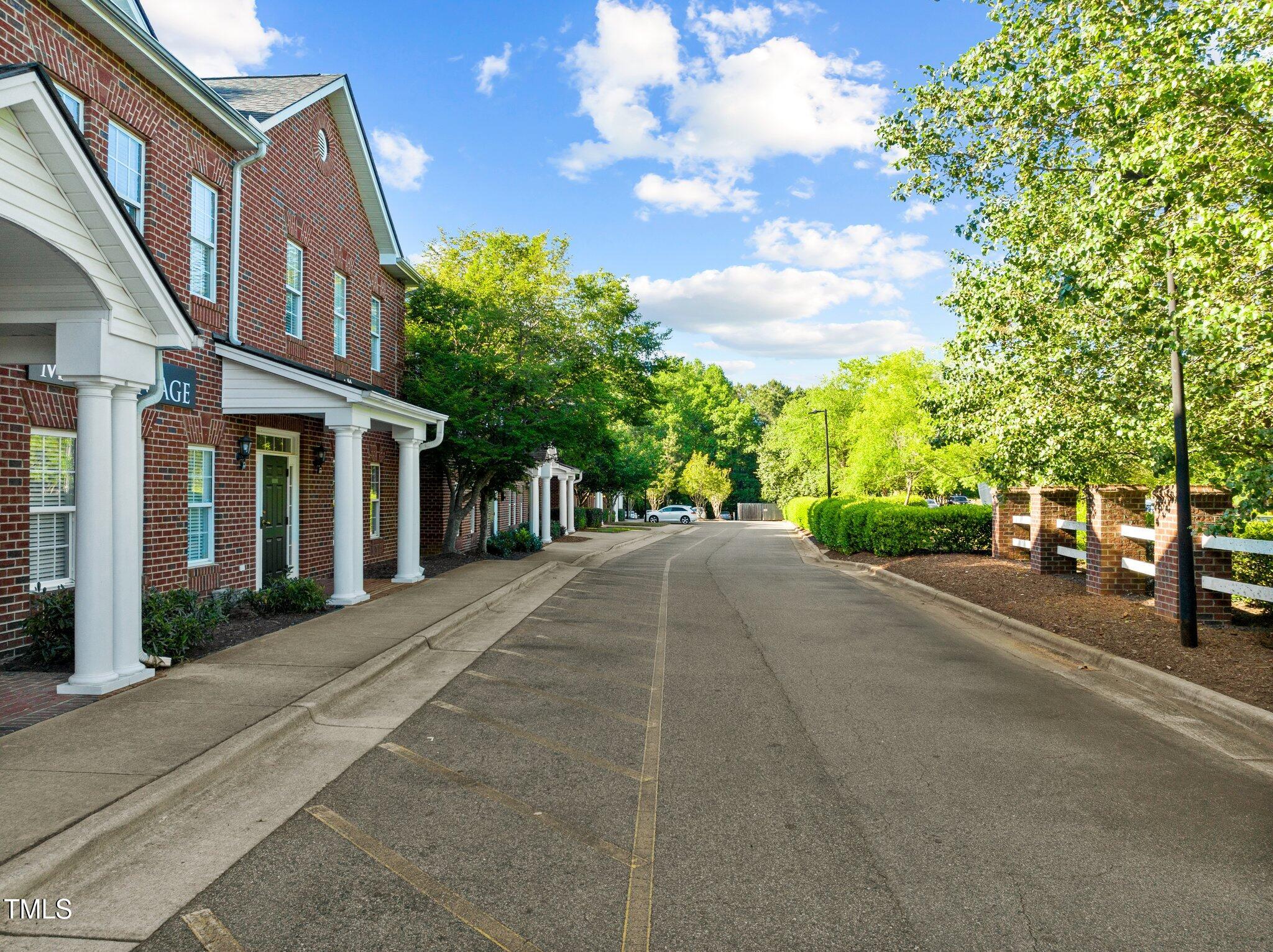 Brick multi-unit building with white entrance columns beside a tree-lined drive.