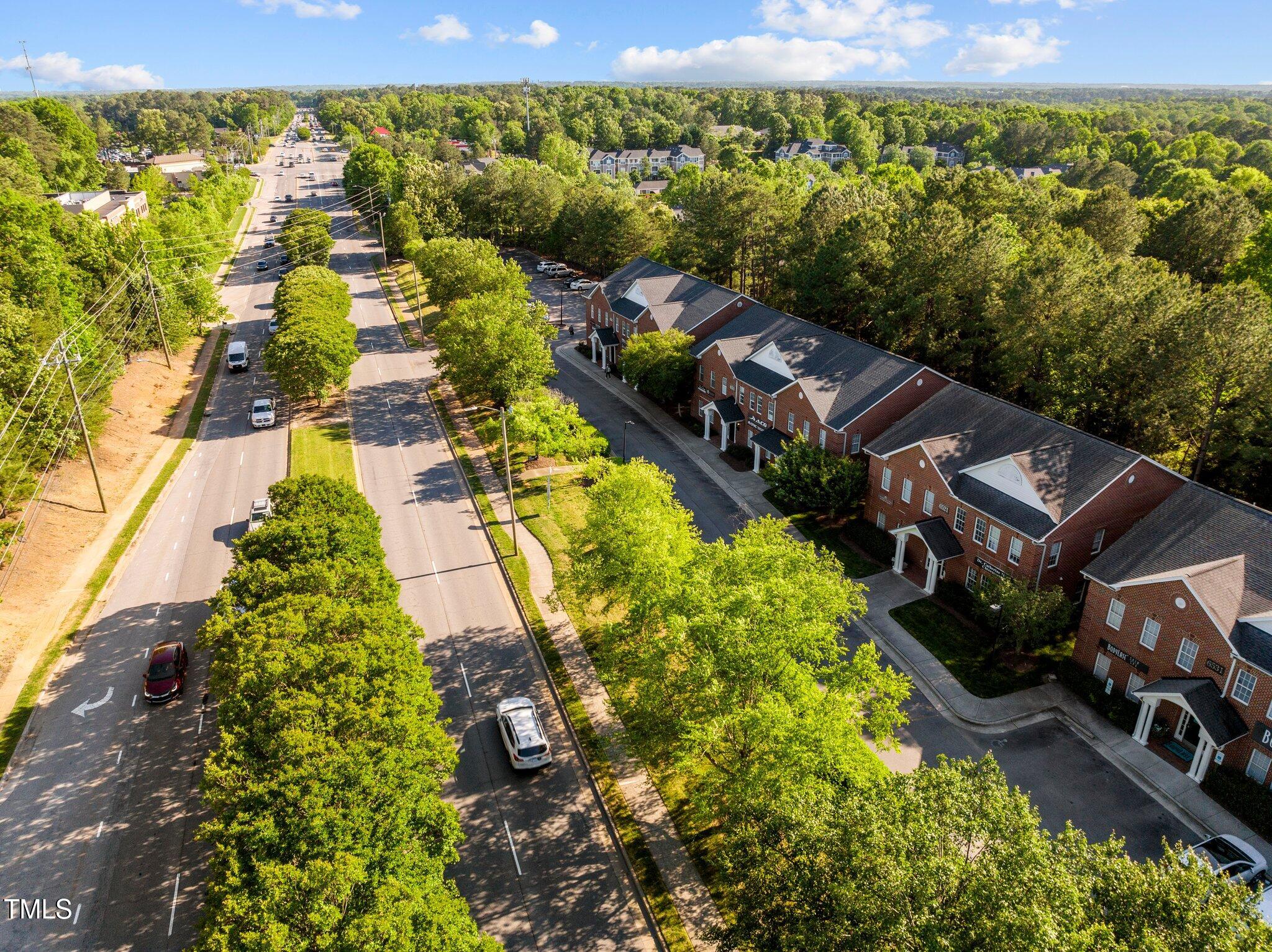 Aerial view of red-brick multi-unit buildings beside a busy road, framed by mature trees.