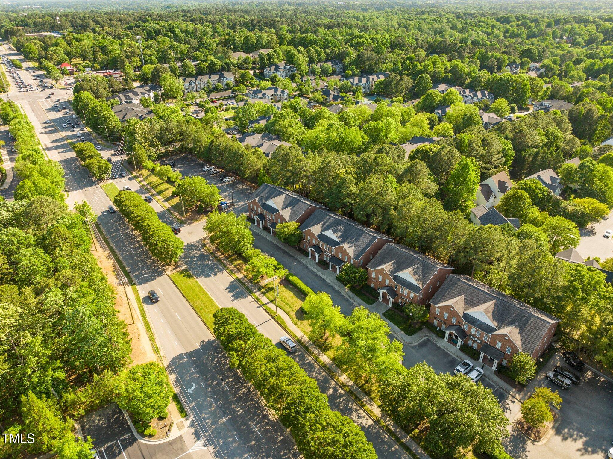 Aerial view of a red-brick multi-unit building beside a tree-lined road and parking lots.