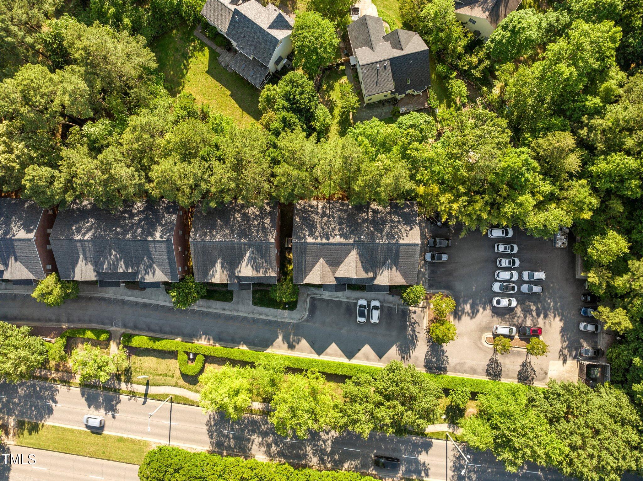 Aerial view of a wooded residential complex with attached buildings and a parking lot.