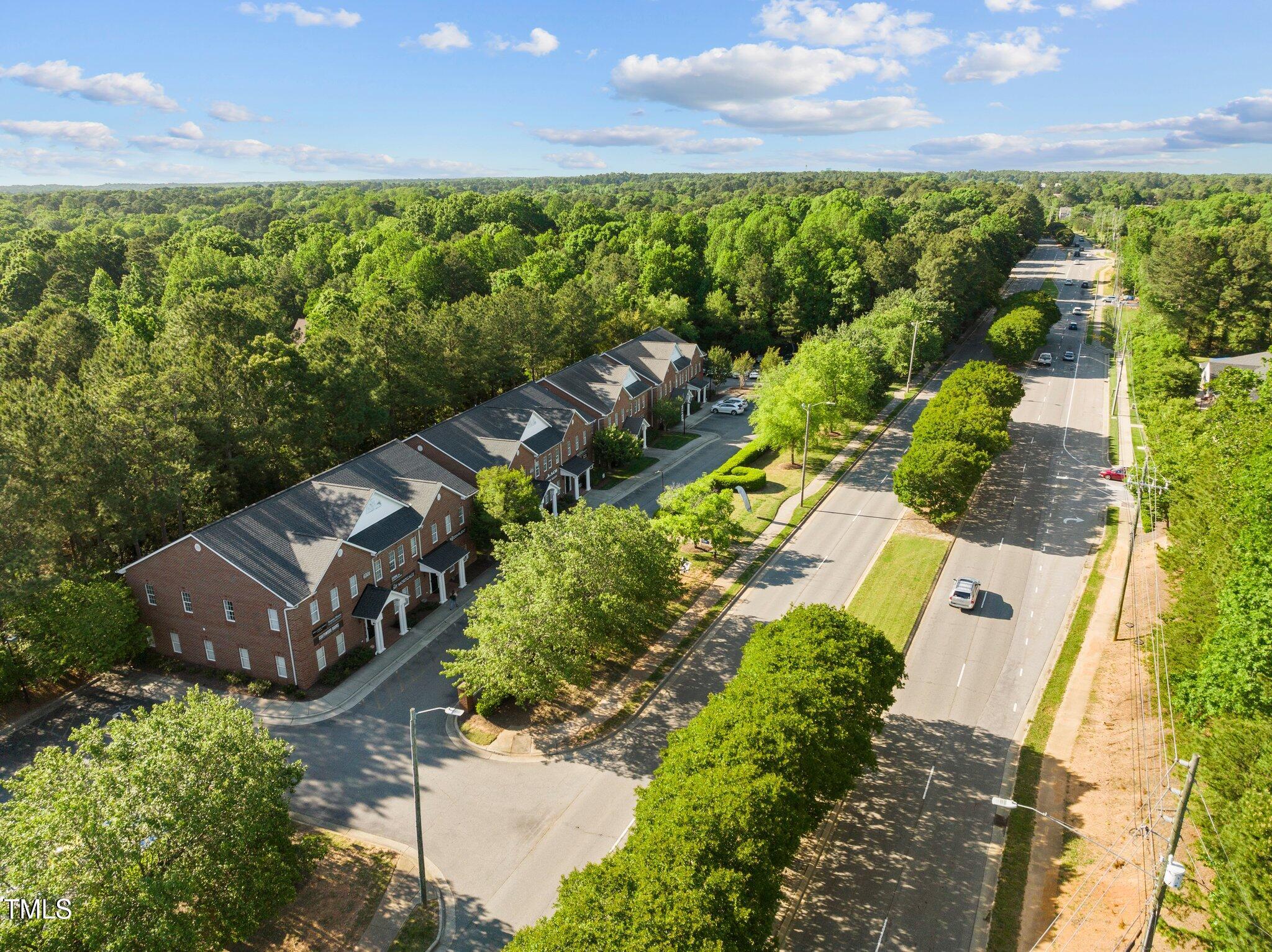 Aerial view of a red-brick multi-unit building beside a tree-lined divided road.