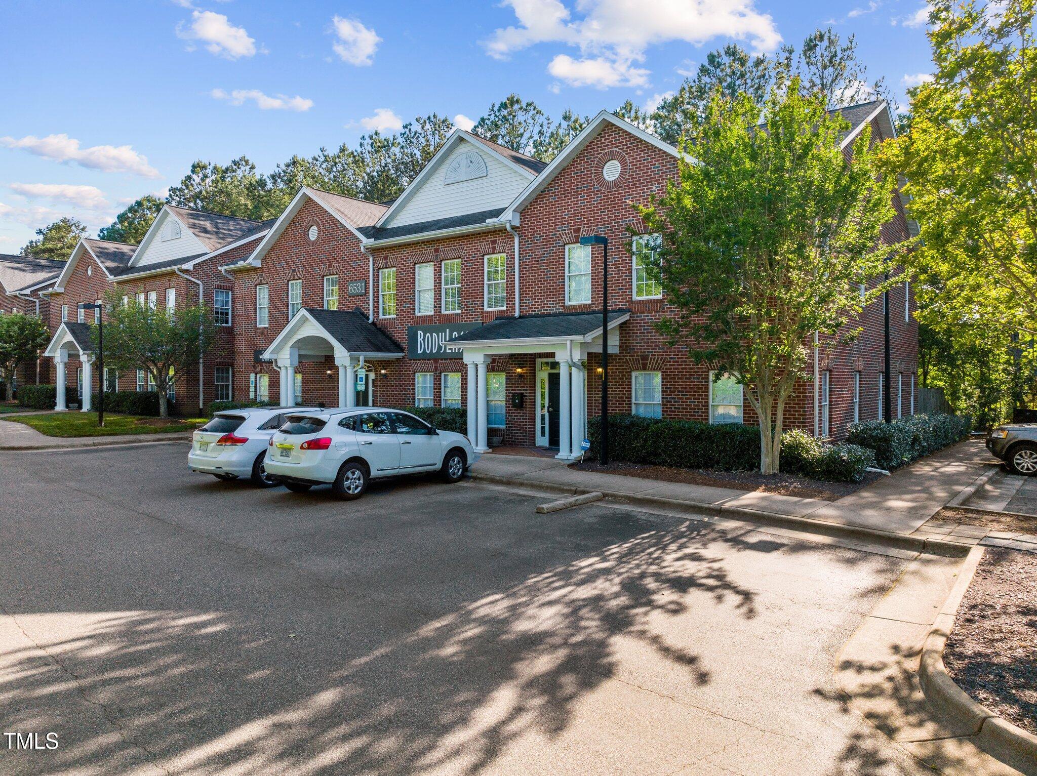 Red-brick multi-unit building with white gables and covered entrances, viewed from the parking area.