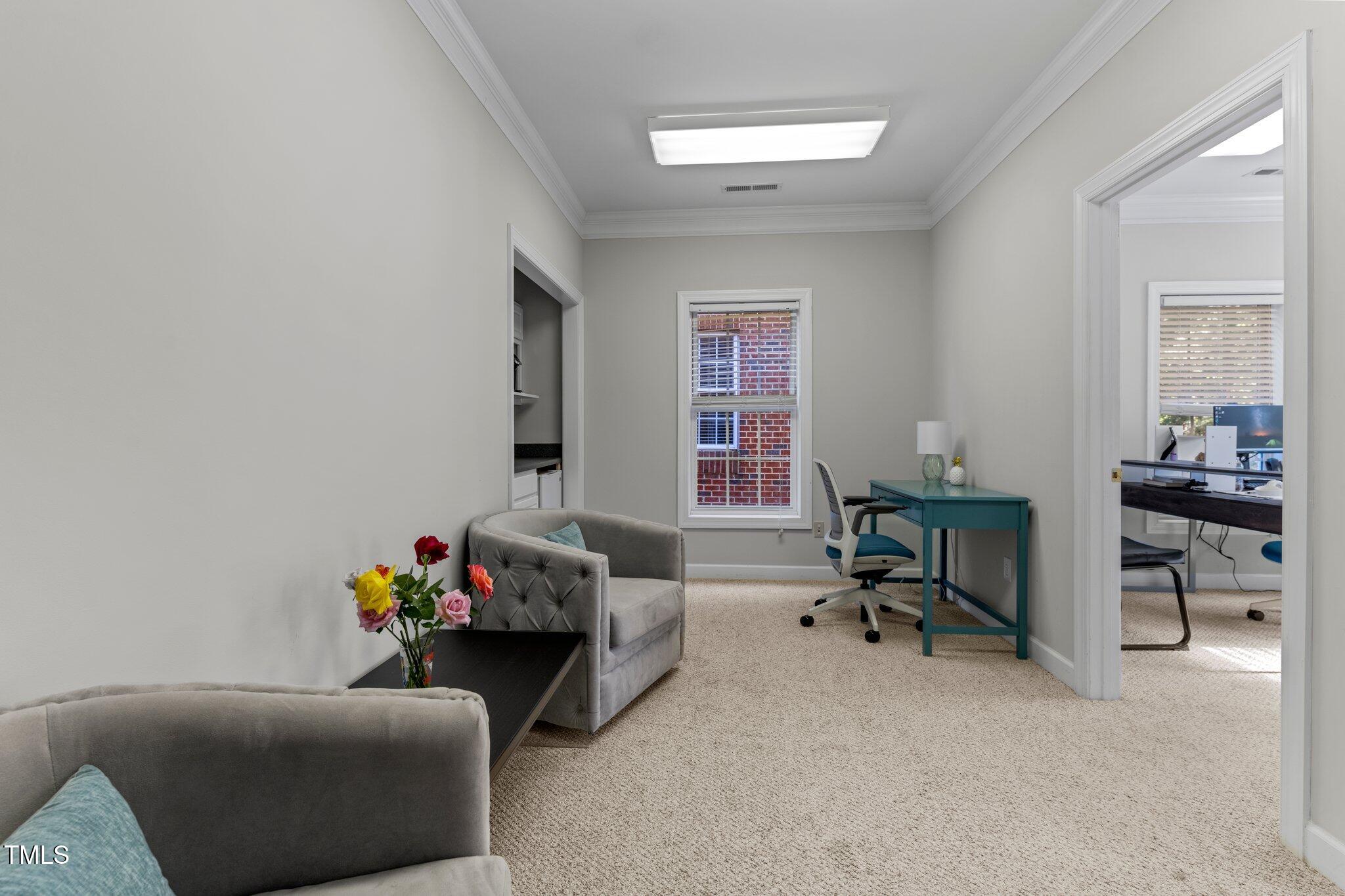 Furnished sitting area and workspace with gray sofas, a teal desk, and a doorway to an adjoining office.