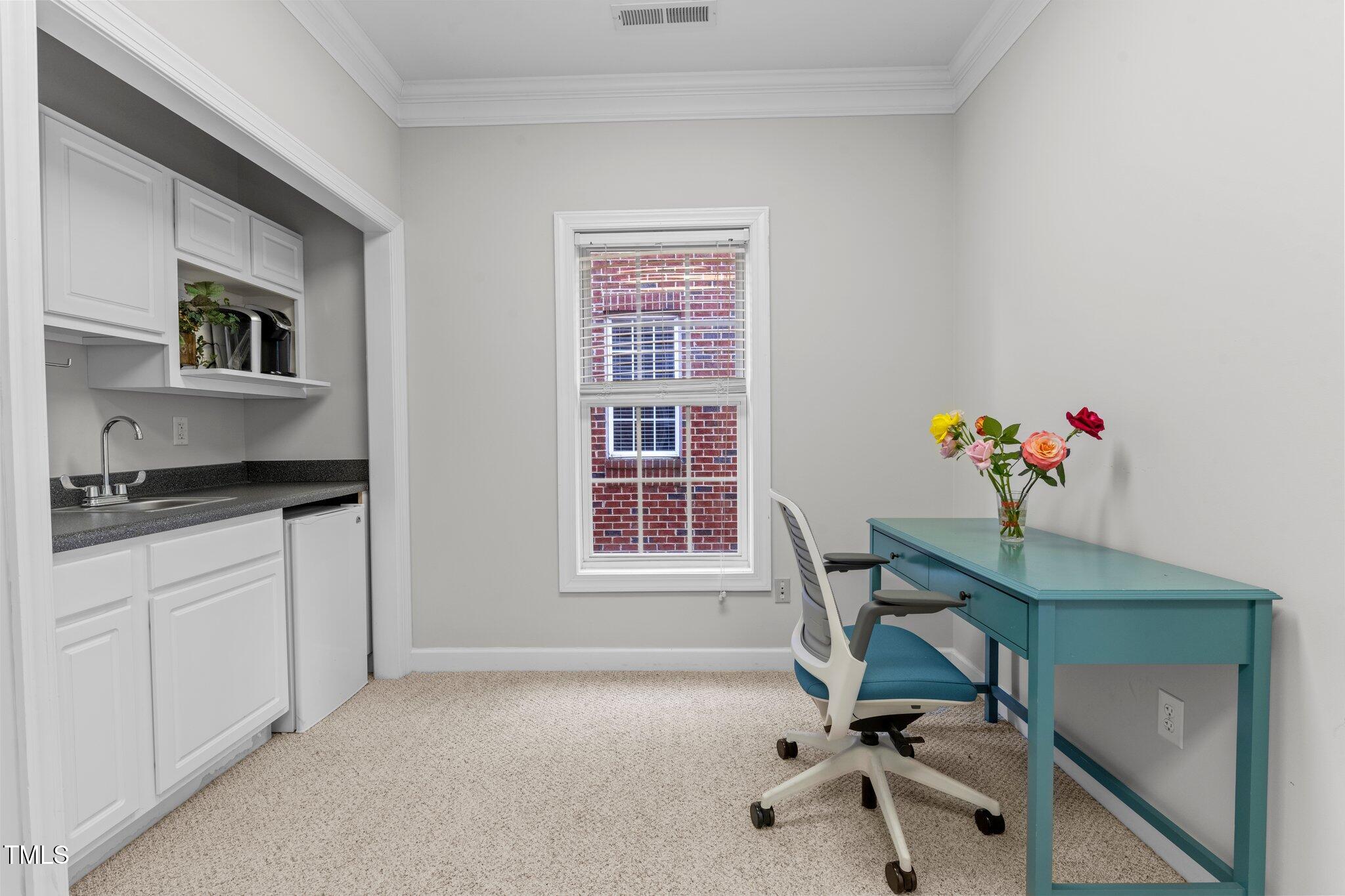 Home office with a turquoise desk and rolling chair, built-in cabinetry, sink, and window.
