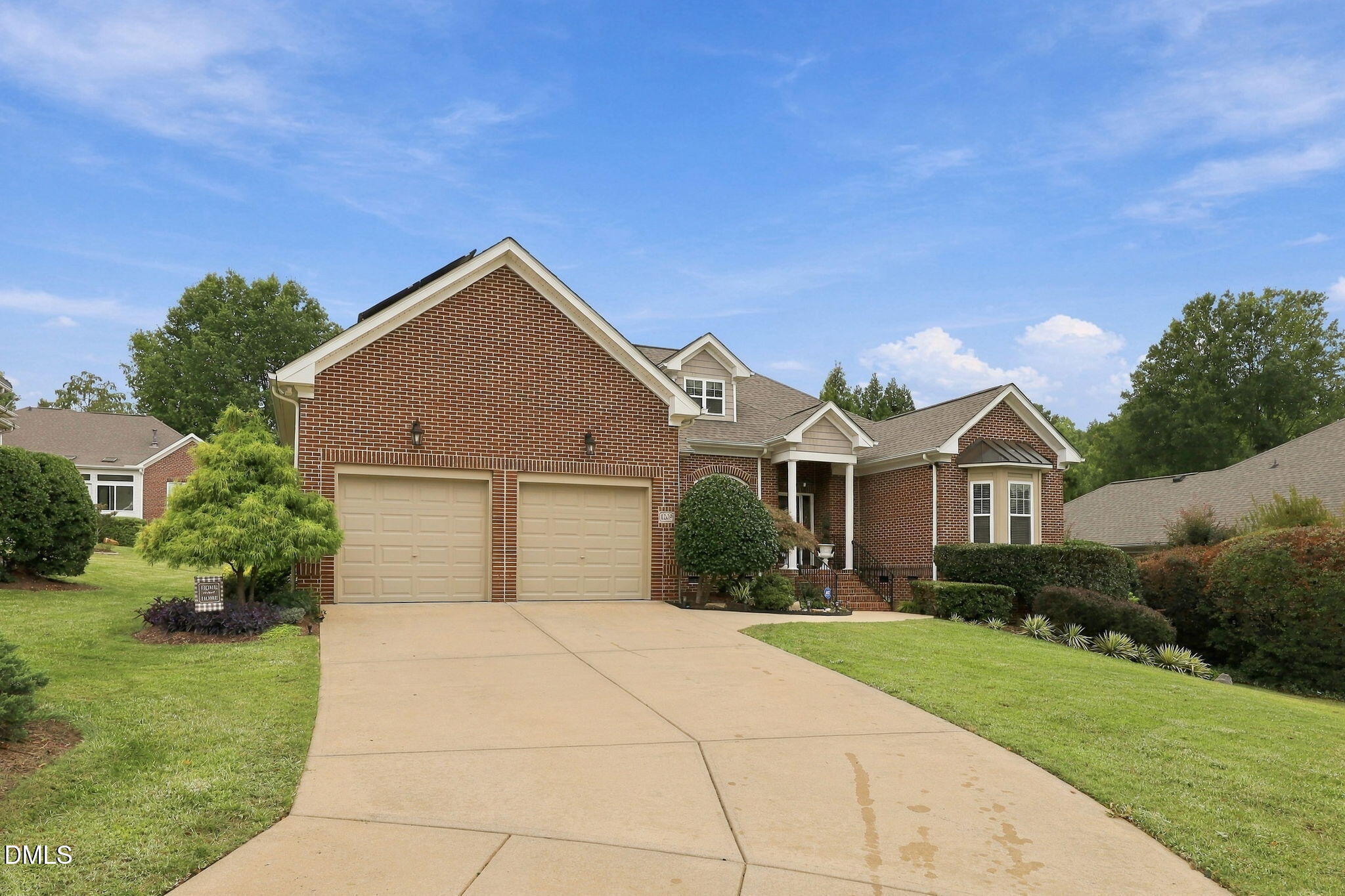 Brick house with double garage, wide driveway, landscaped lawn, and covered front entry.