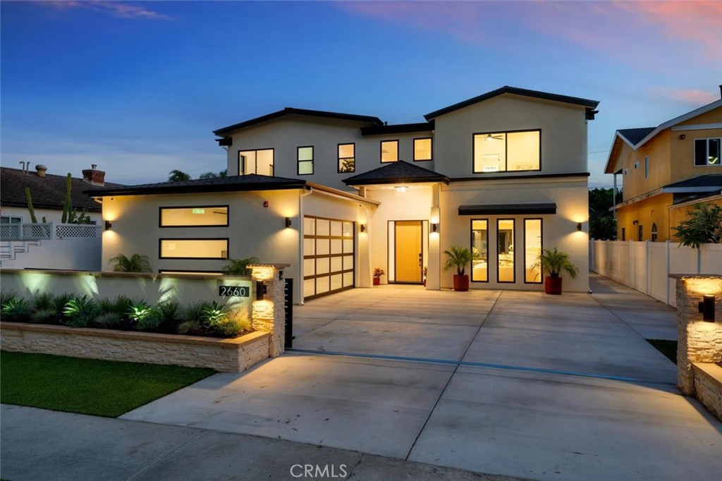 Modern two-story home at dusk with glowing windows, a wide driveway, and landscaped entry.
