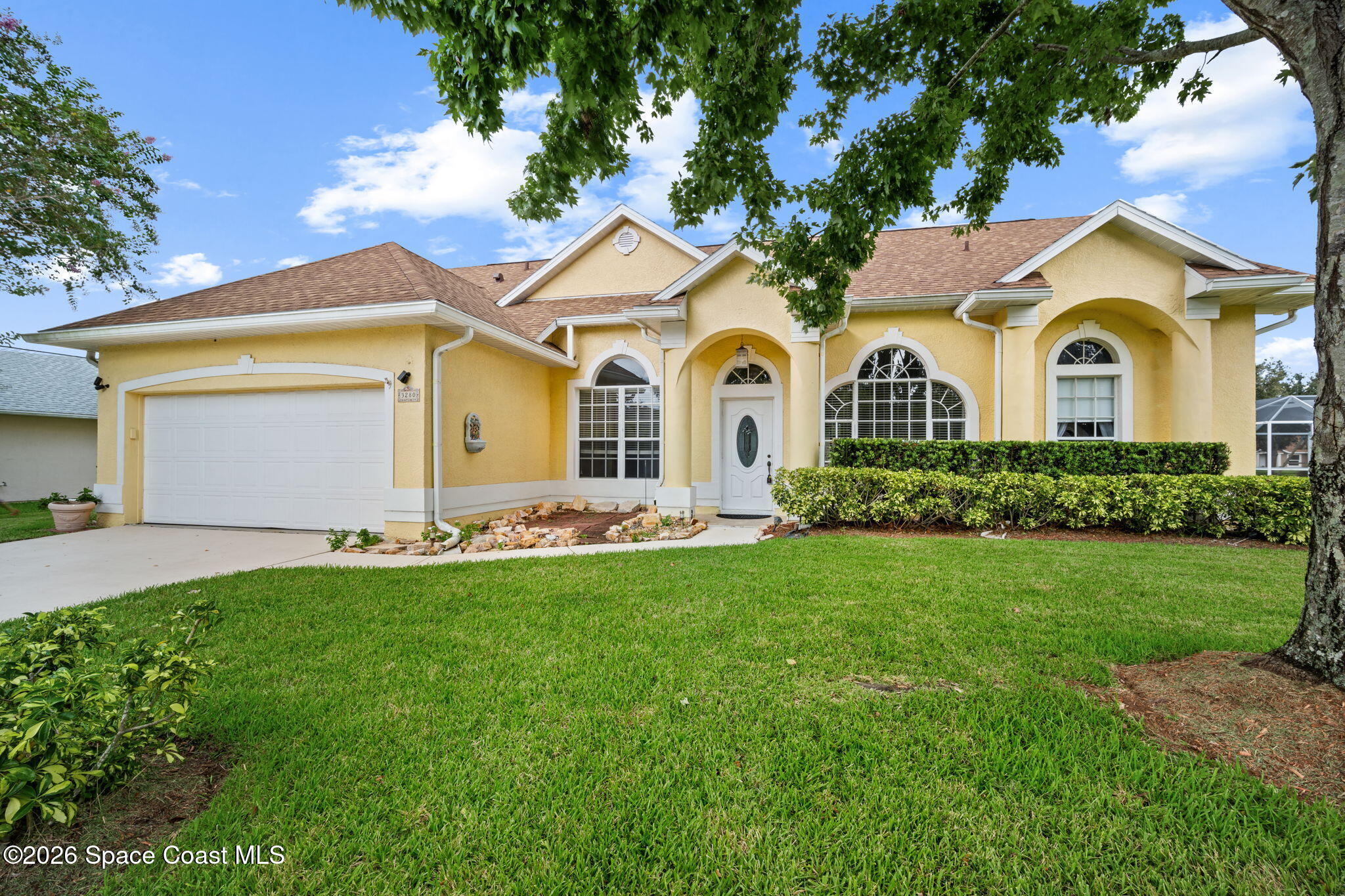 Yellow stucco home with arched windows, a white garage door, and a landscaped front lawn.