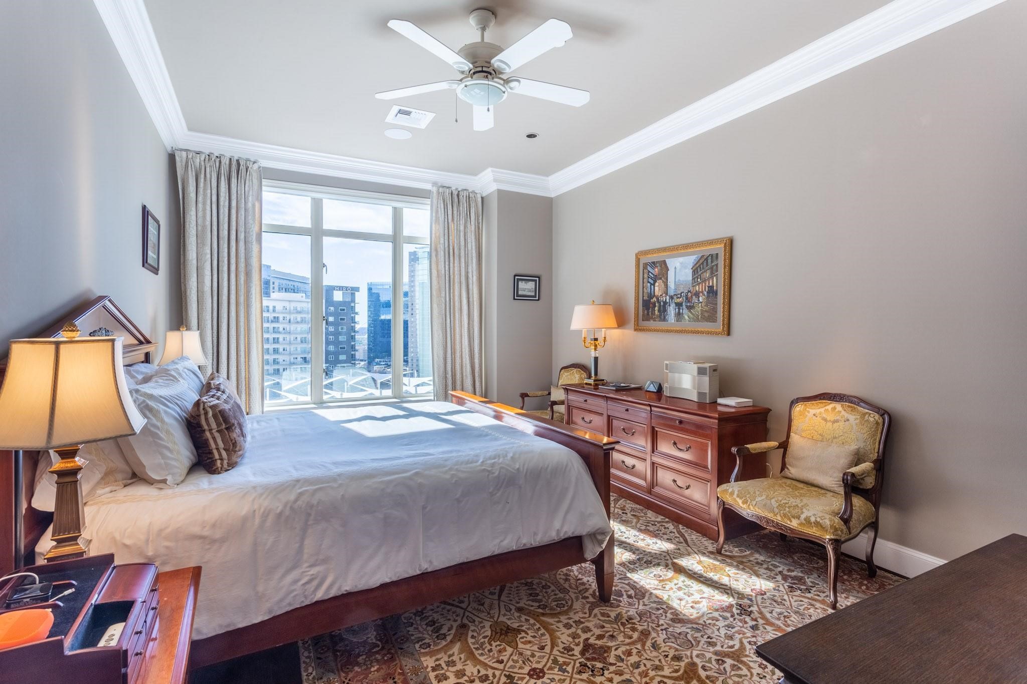 Furnished bedroom with a large bed and city views through floor-to-ceiling windows.